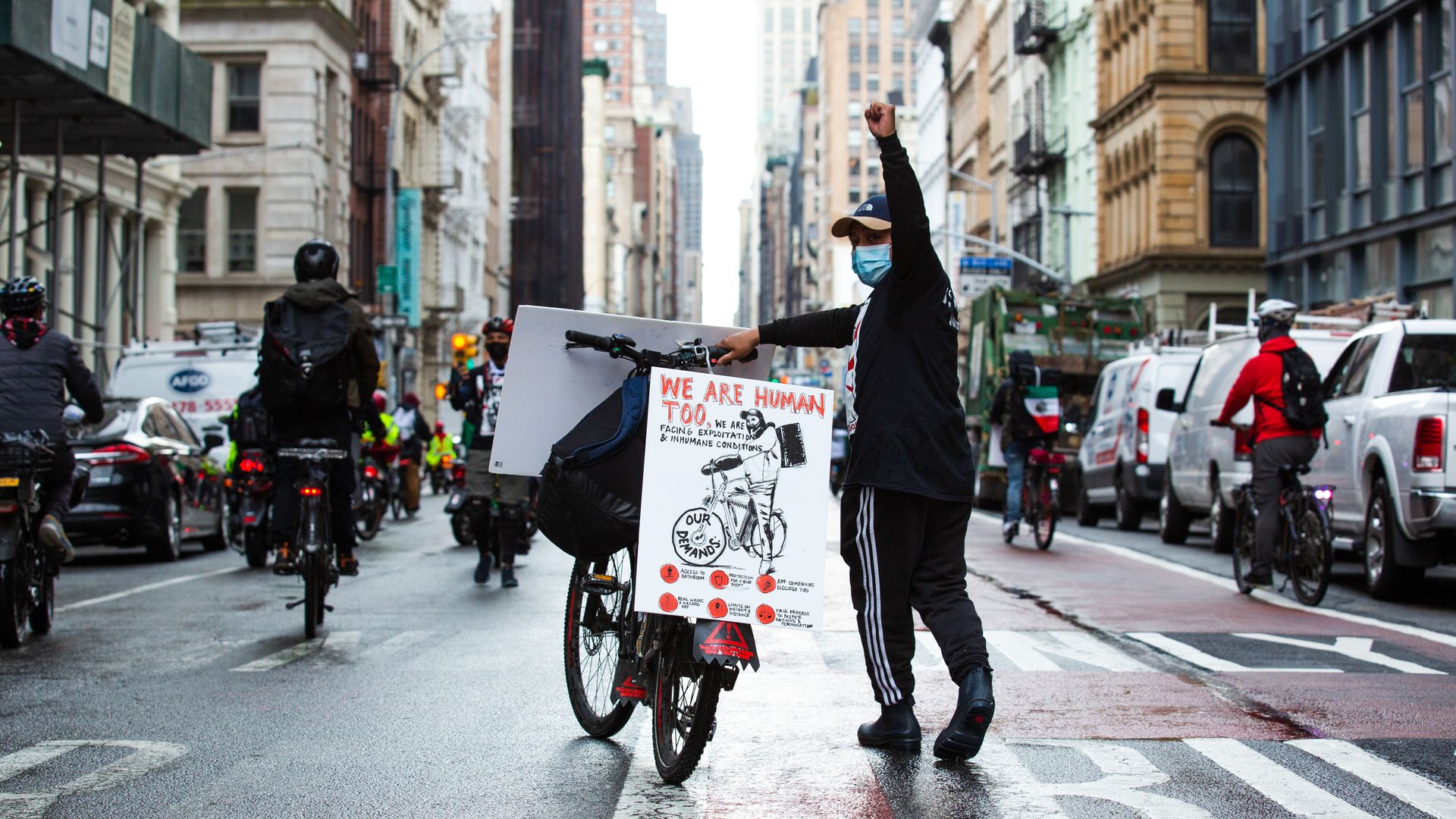 A delivery worker raises their fist in the middle of a street.