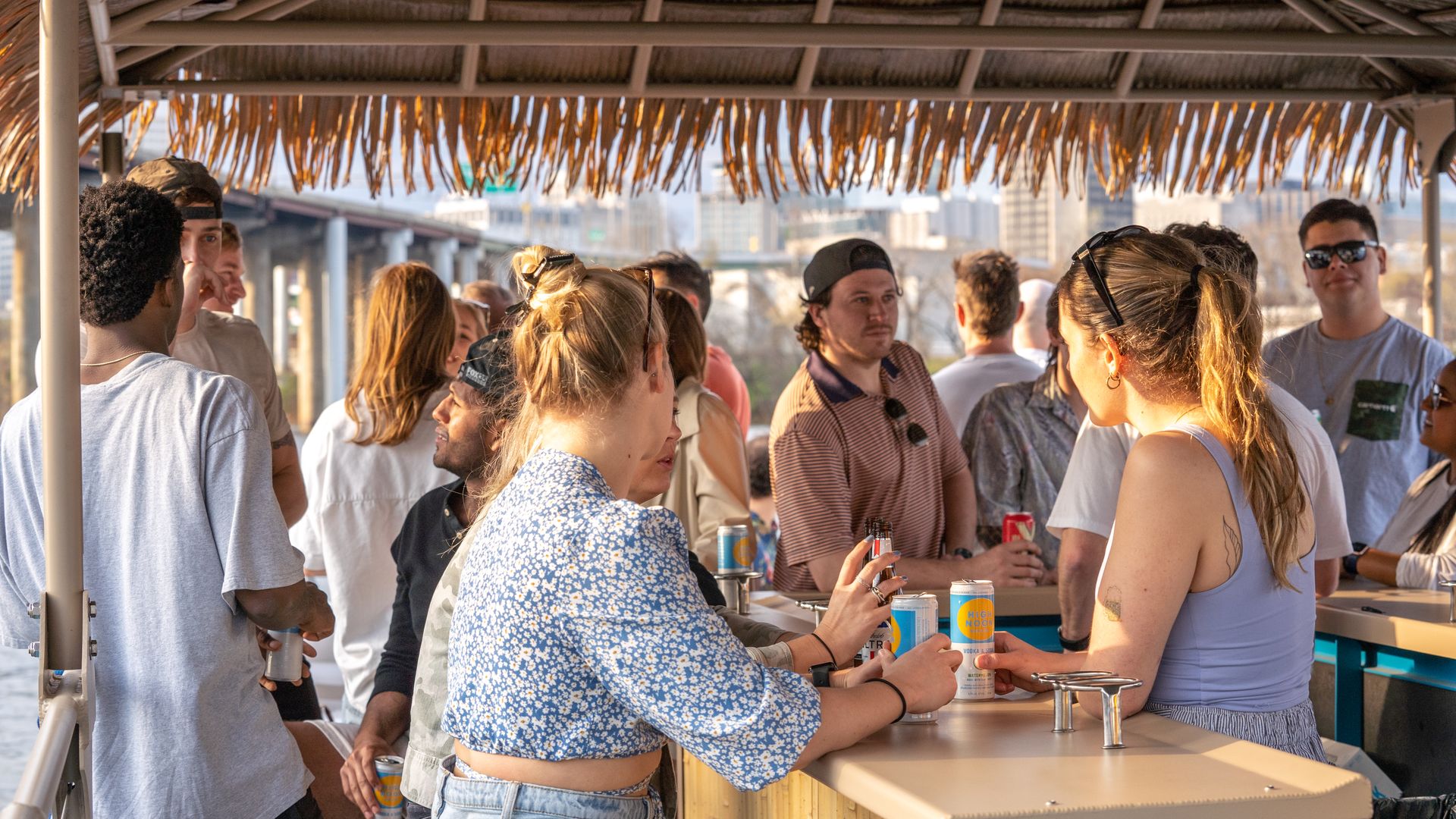 People standing and drinking on a boat with a tiki hut