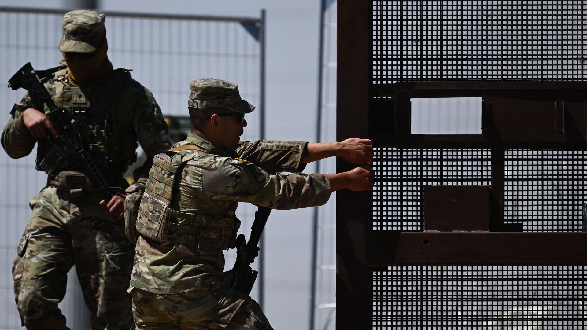 A member of the Texas Army National Guard closes a gate on the border wall as US Customs and Border Protection Border Patrol agents search migrants surrendering themselves for the processing of immigration and asylum claims on the US-Mexico border in El Paso, Texas 