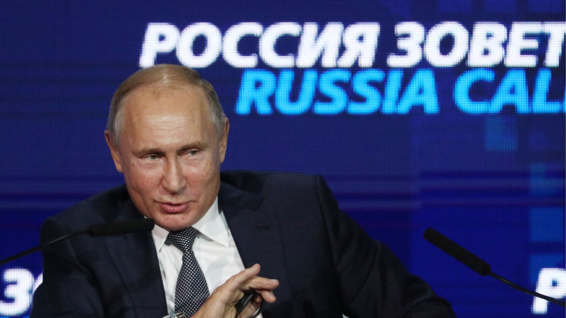 Vladimir Putin smiles and gestures.