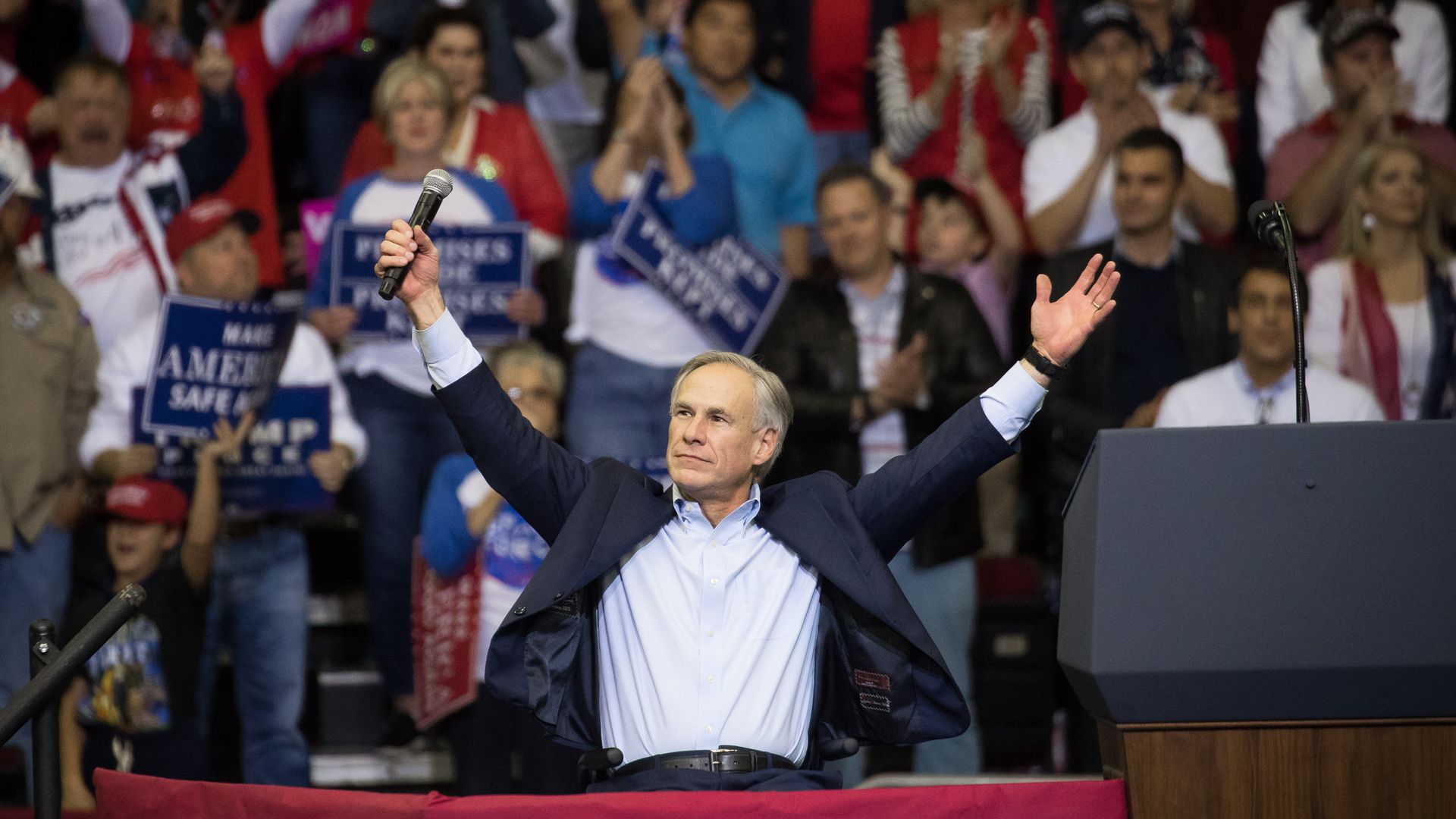 Greg Abbott at a rally, holding his hands up victoriously.