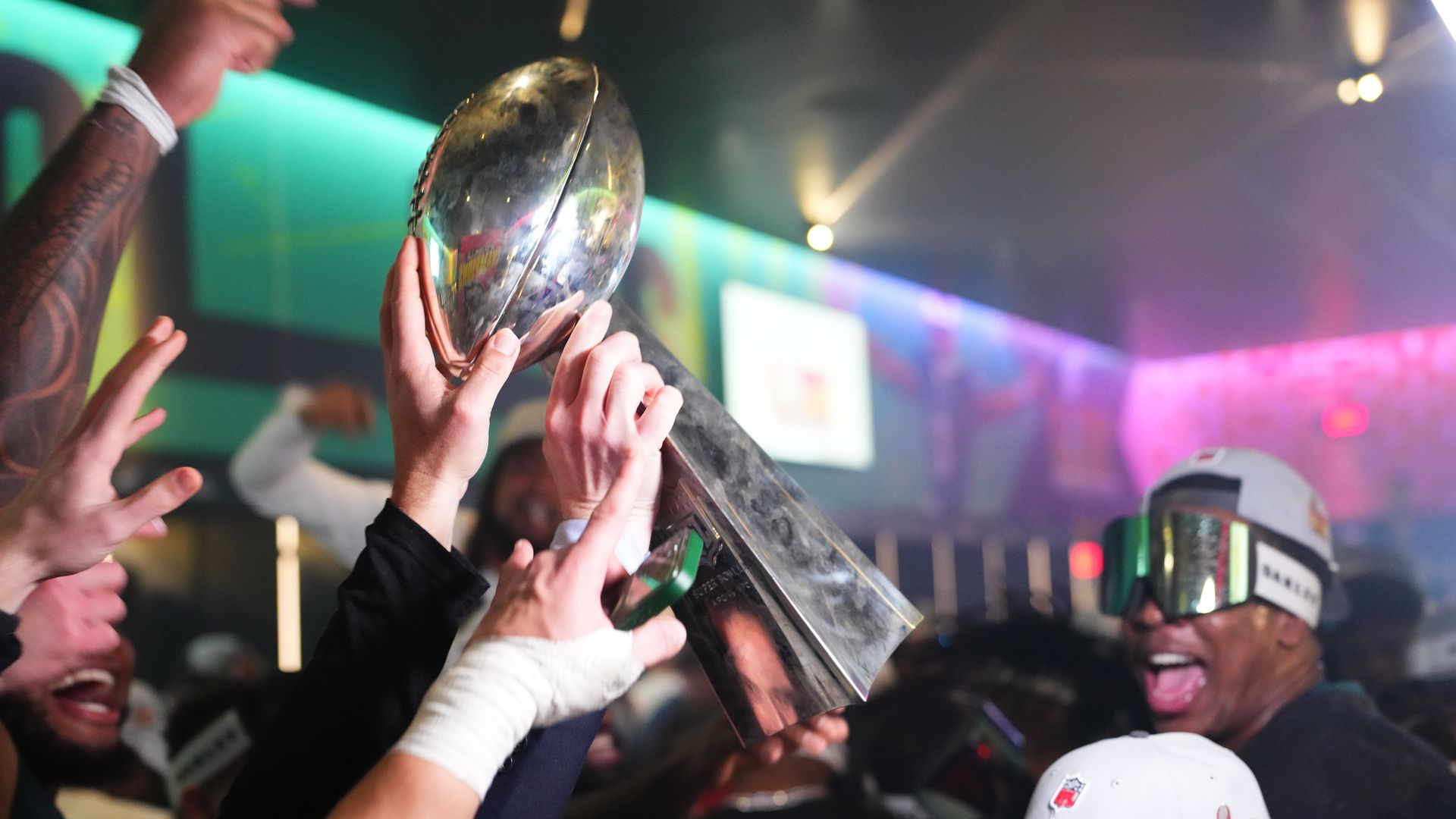 Hands touch the Super Bowl trophy at a locker room celebration.