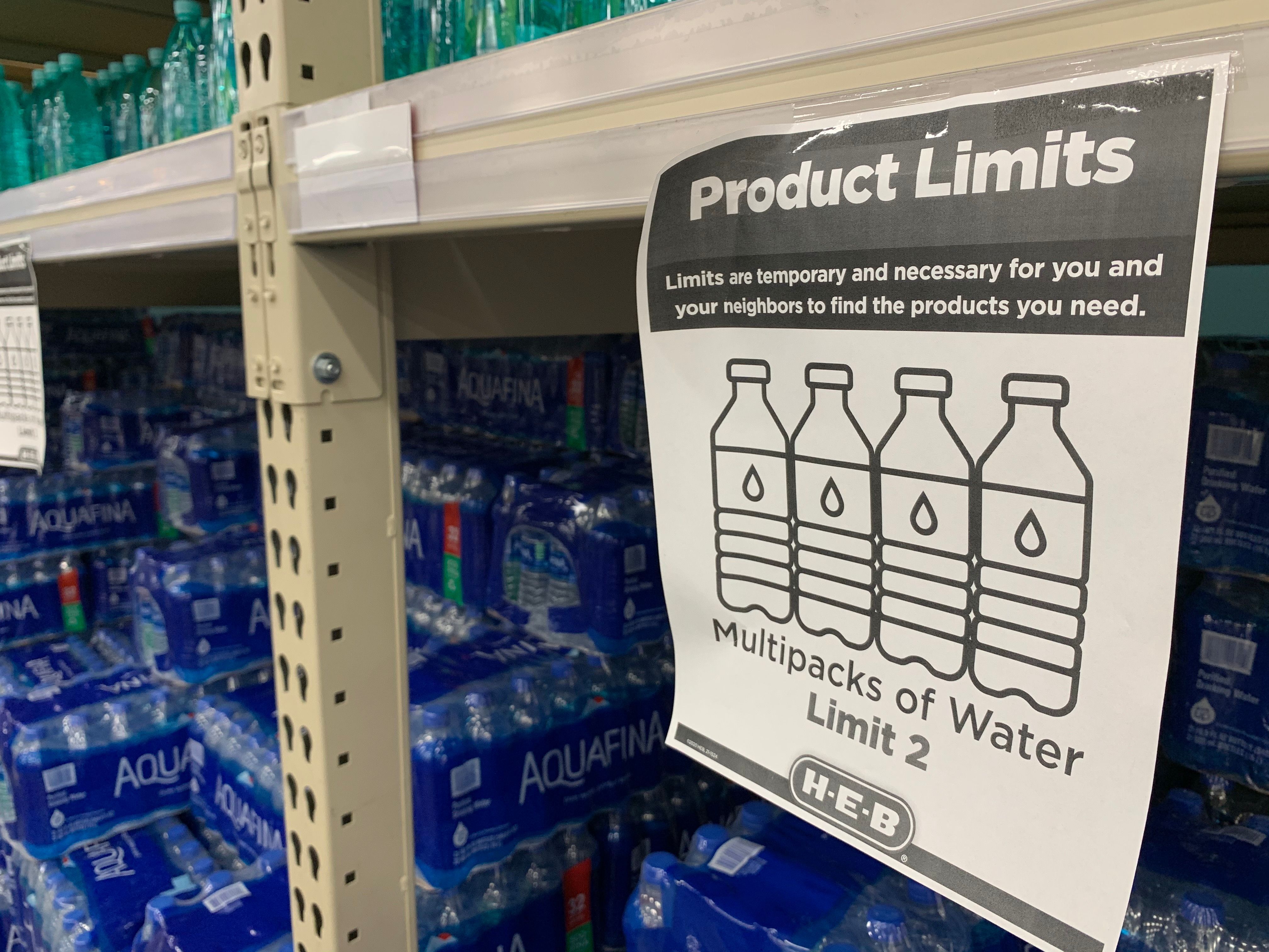 A sign attached to a shelf in front of packs of water reads "product limits. Multipacks of water limit 2"