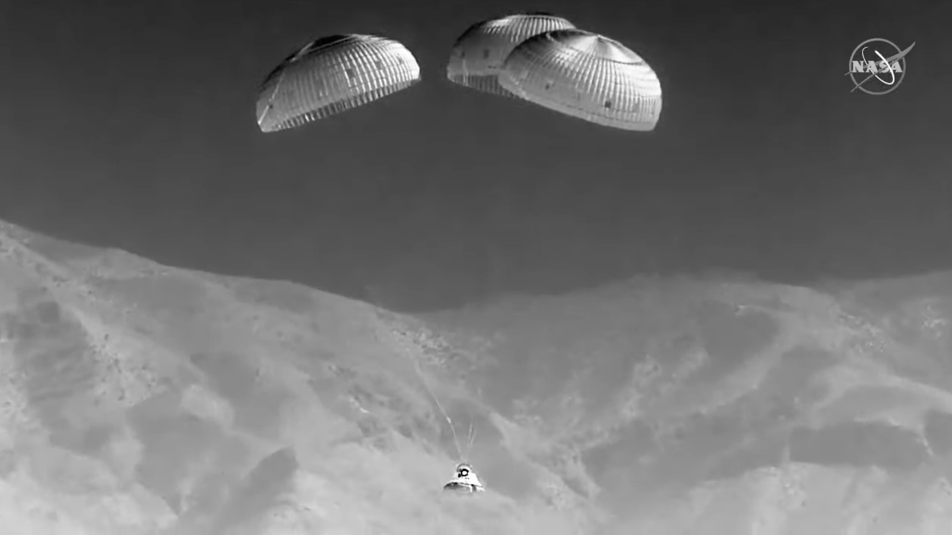 Starliner coming back to Earth in black and white with mountains behind it