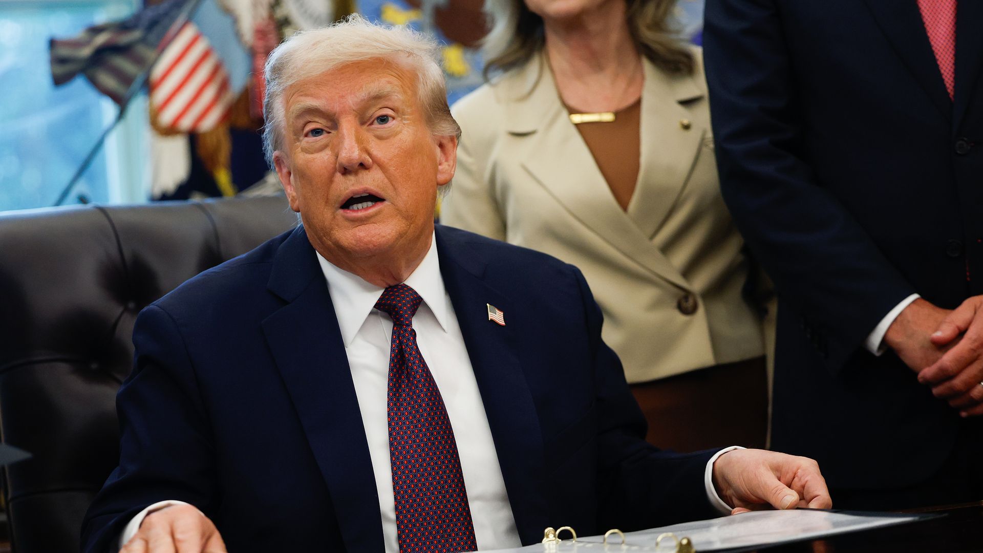 President Trump seated at the Resolute Desk in the Oval Office, with papers in front of him.
