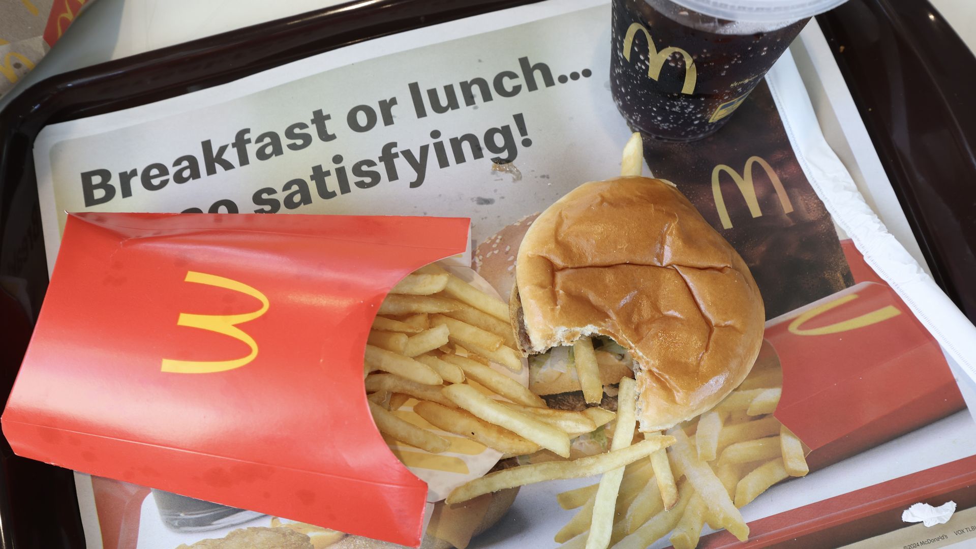 McDonald's meal on a tray with a bite-taken hamburger, red fries container spilling fries, and a cup of soda with McDonald's logo.
