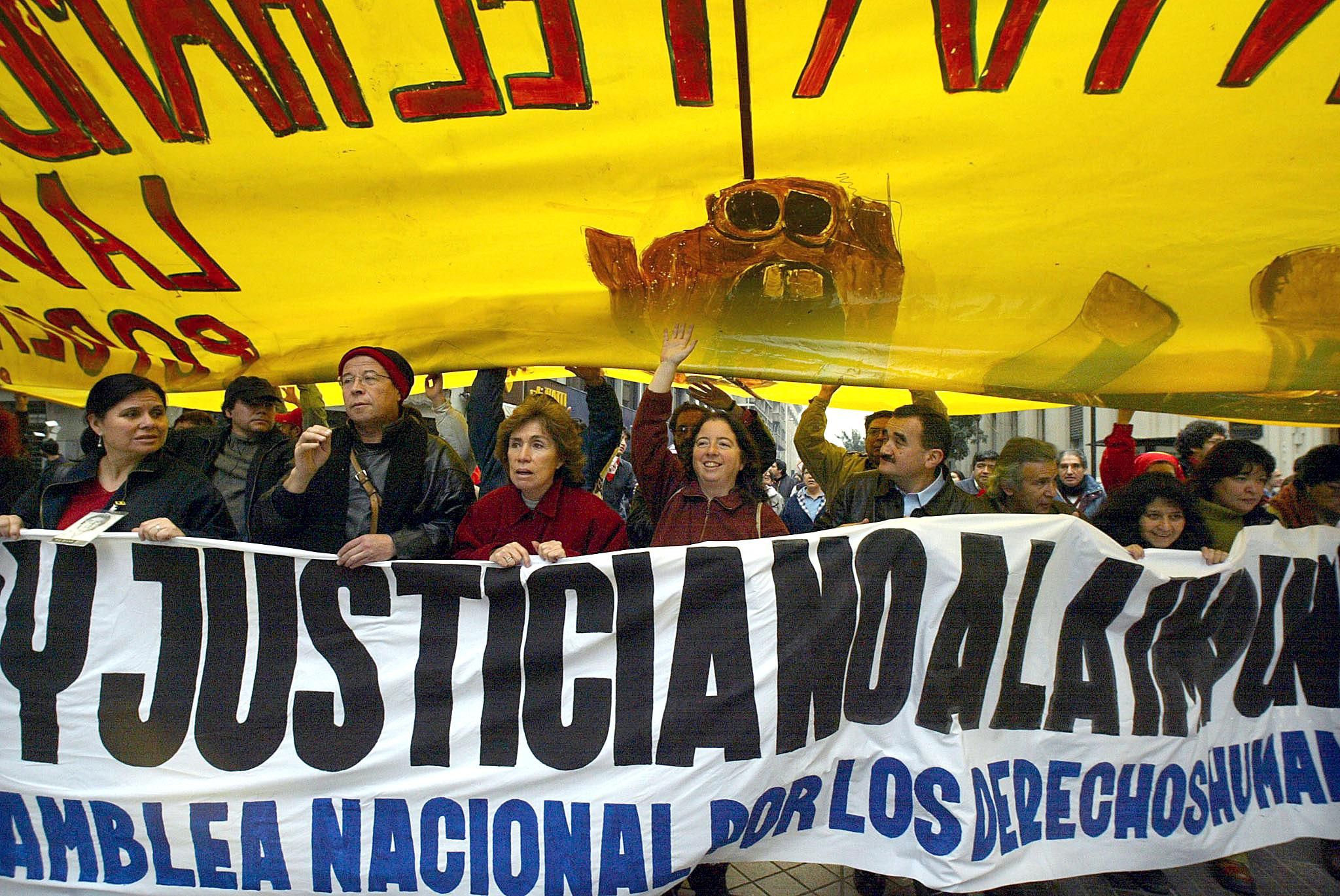 Protesters carry a large white banner in Spanish letters as a larger yellow banner hangs over them in Chile in  2002