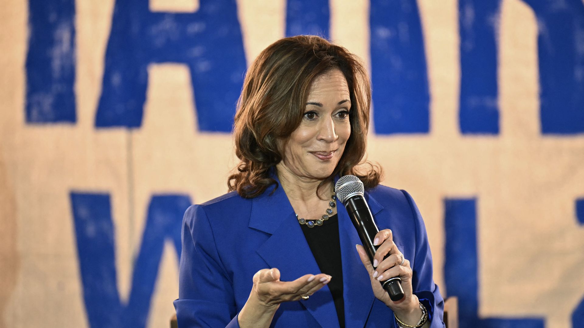 Kamala Harris holds a microphone and gestures with her right hand.