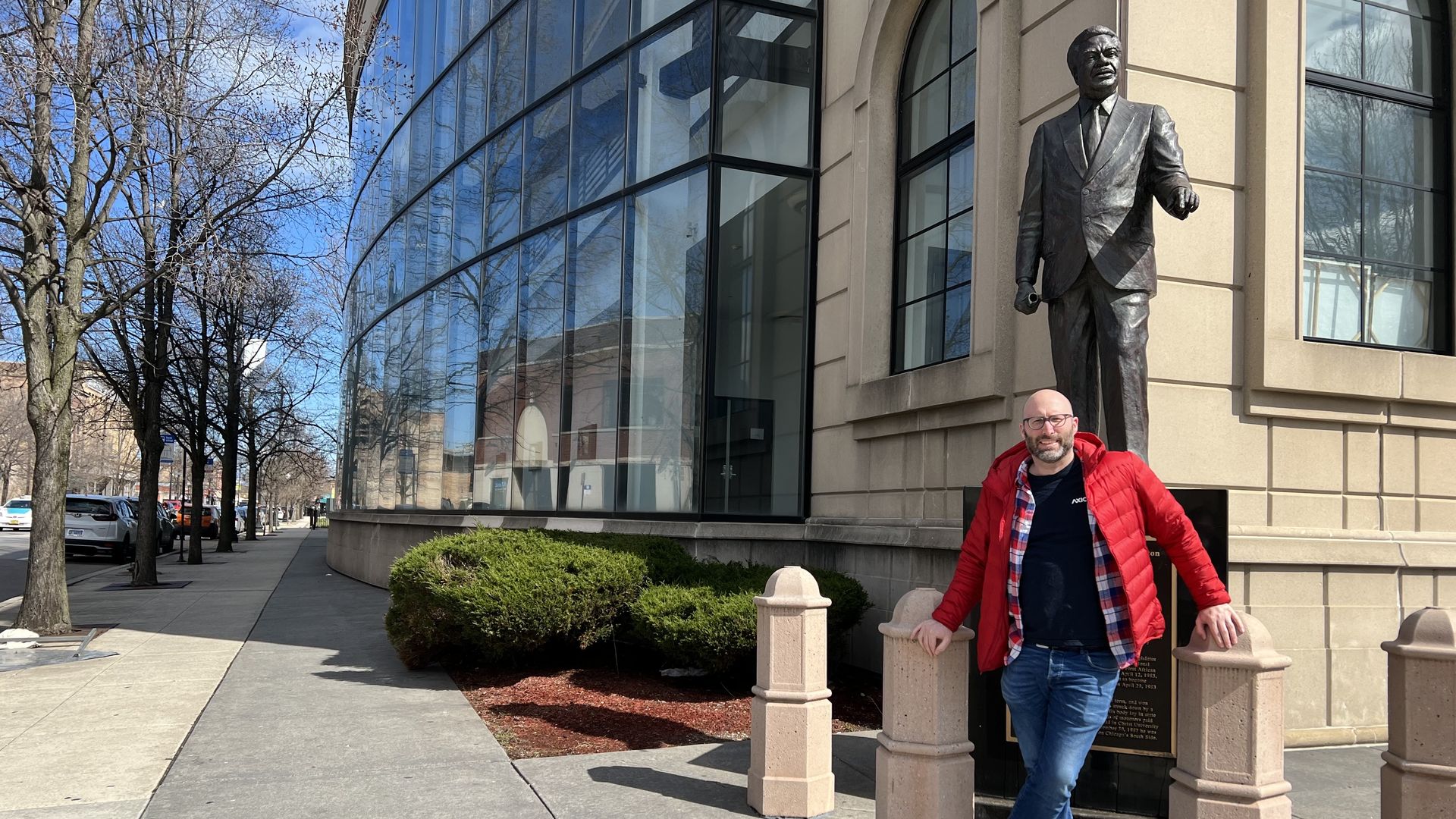 Photo of a man standing in front of a statue and building. 