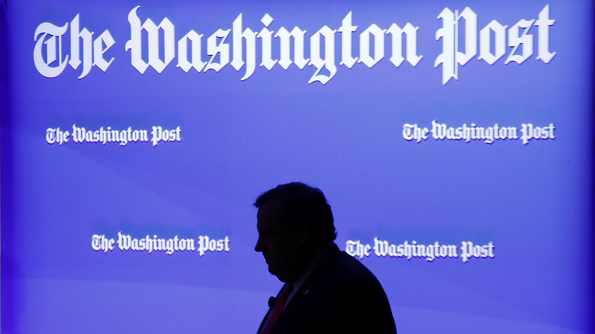 Silhouette of a man before wall with logos of The Washington Post.