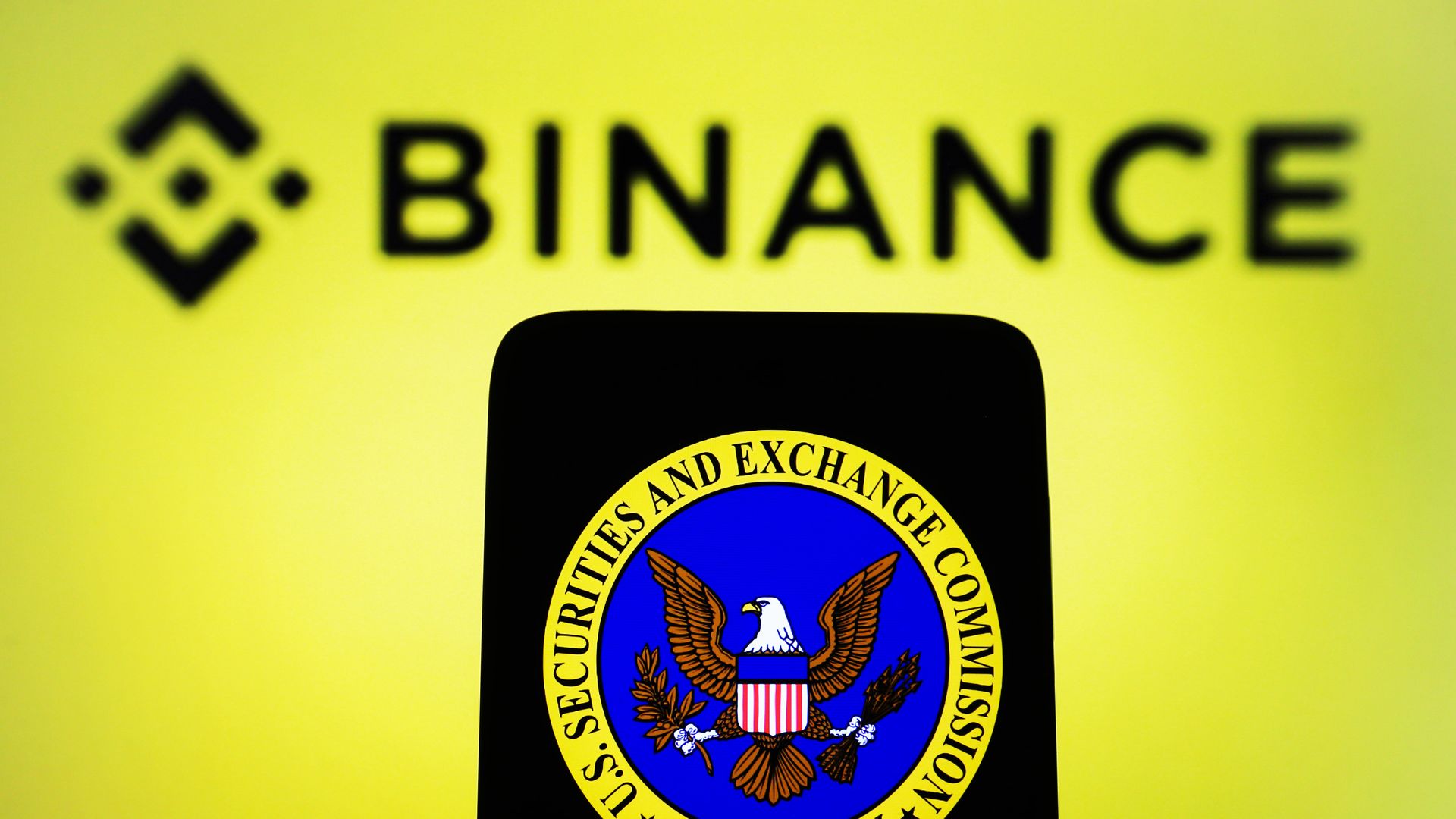 A photo illustration of an SEC logoon a smartphone and Binance logo on a pc screen.