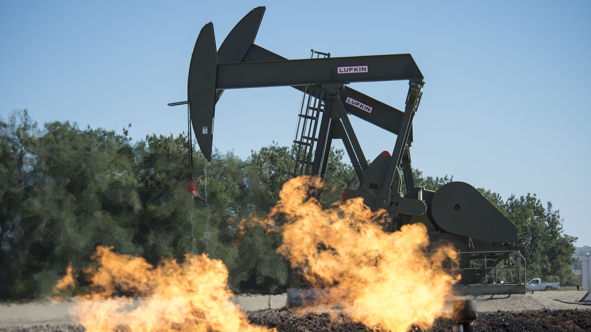 A gas drilling rig with flames from flaring gas coming up from the ground.