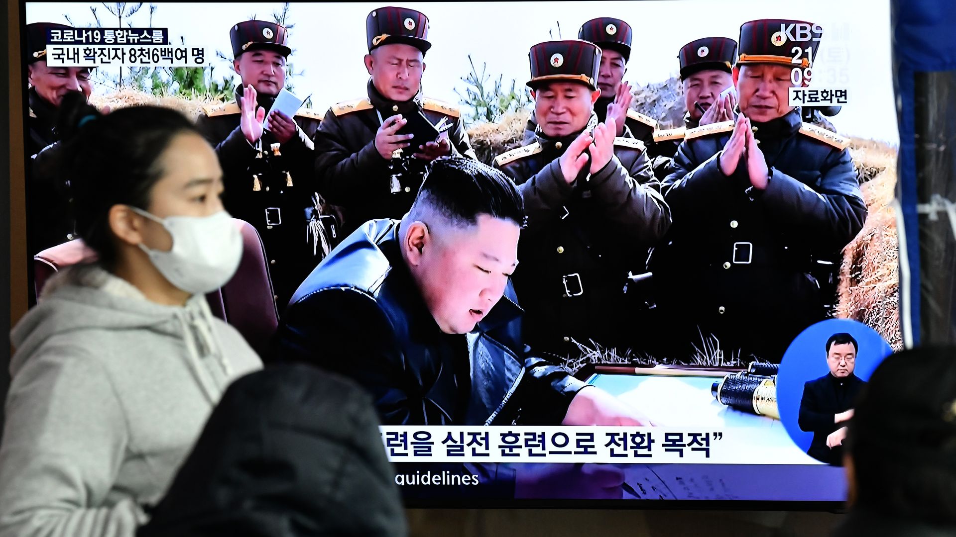  A woman wearing a face mask walks past a television news screen showing a file image of North Korean leader Kim Jong Un, at a railway station in Seoul on March 21