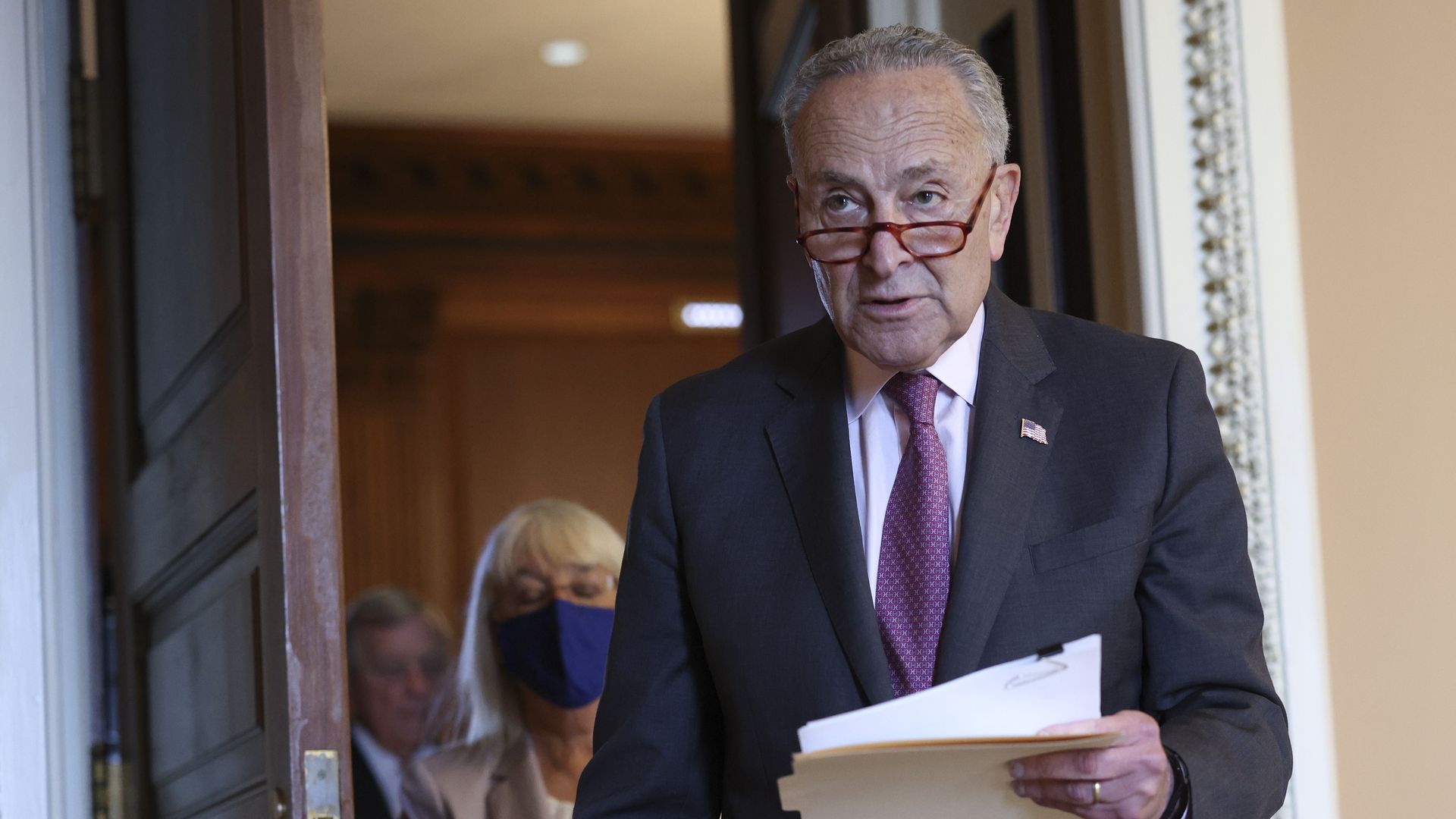 Majority Leader Chuck Schumer walks through door holding papers