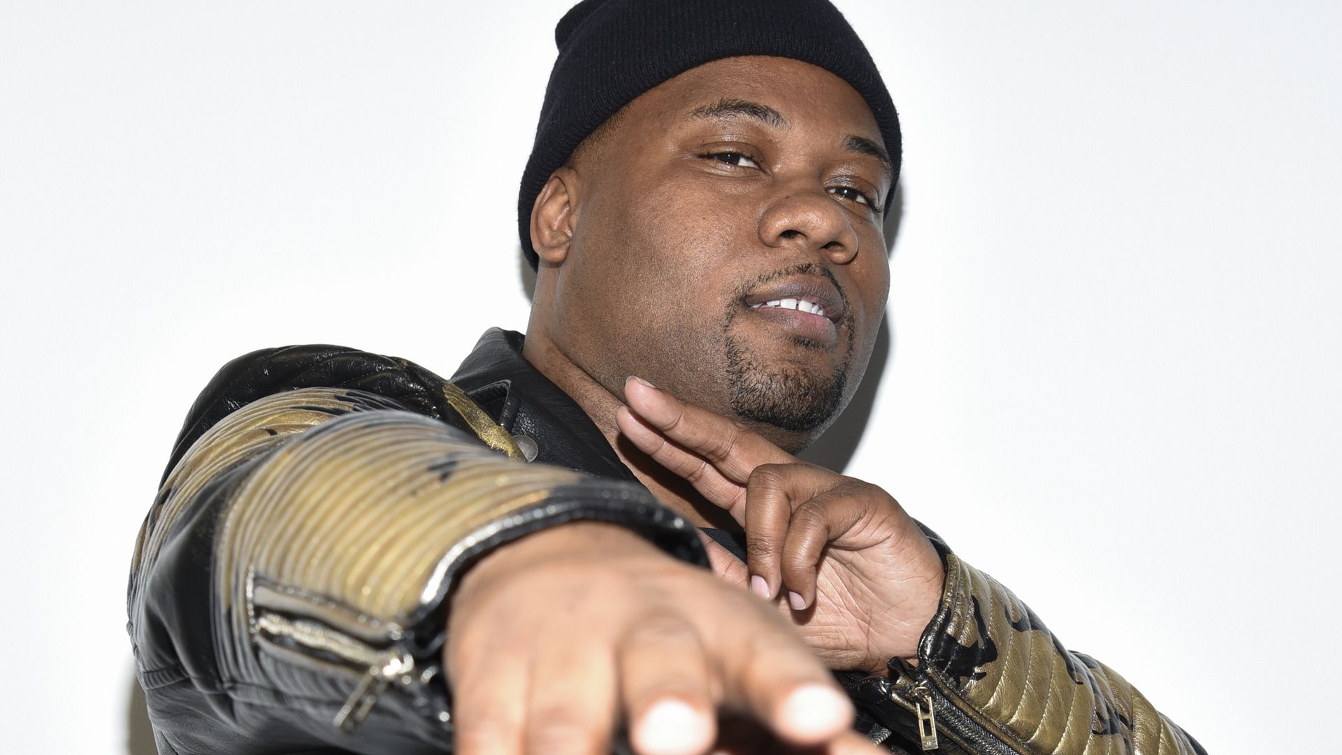 A Black man in a winter hat and leather jacket poses for a photo. 
