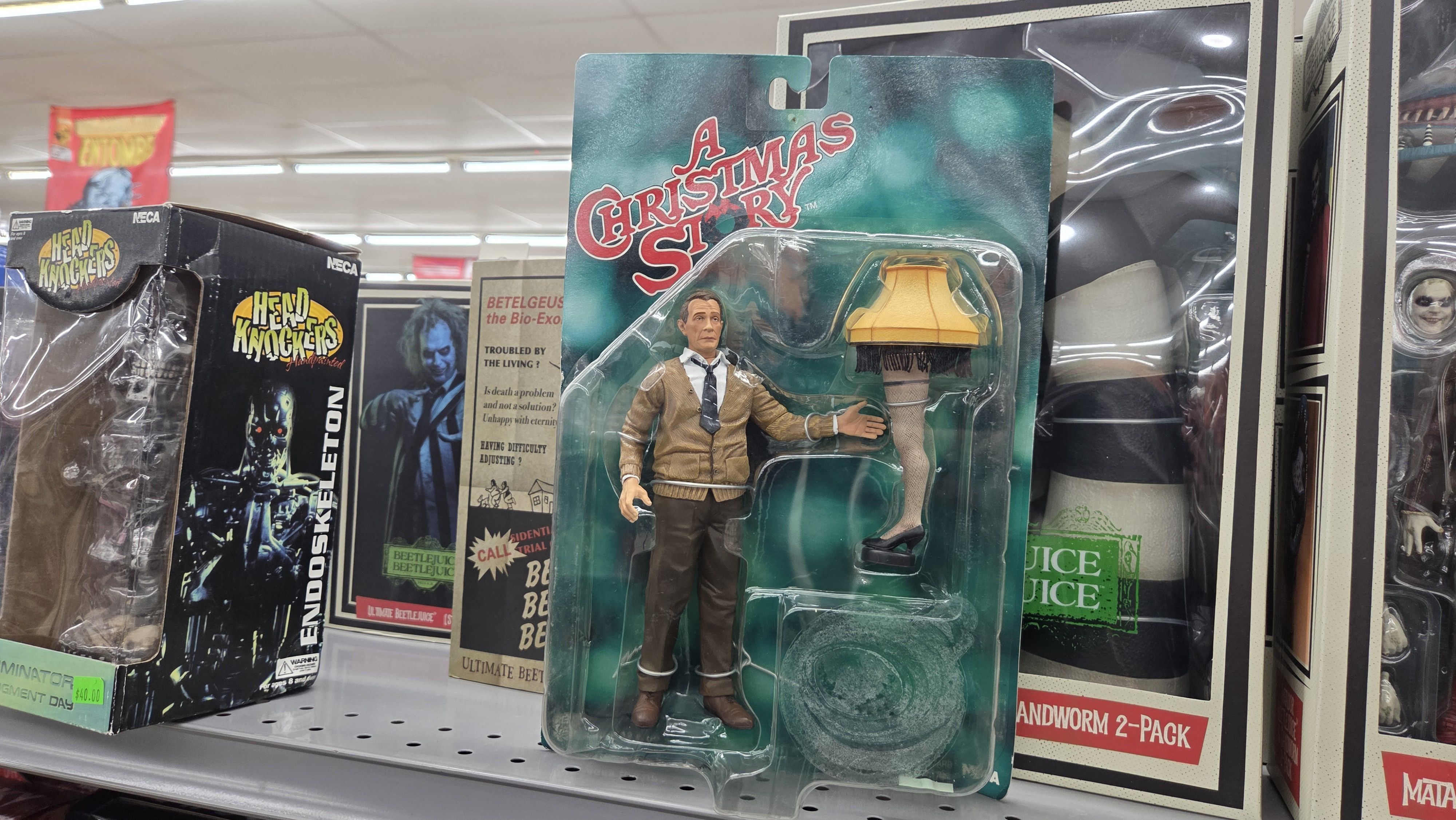 Action figure of Ralphie in a brown sweater from "A Christmas Story" with the iconic leg lamp, displayed in packaging on a shelf with other movie collectibles.