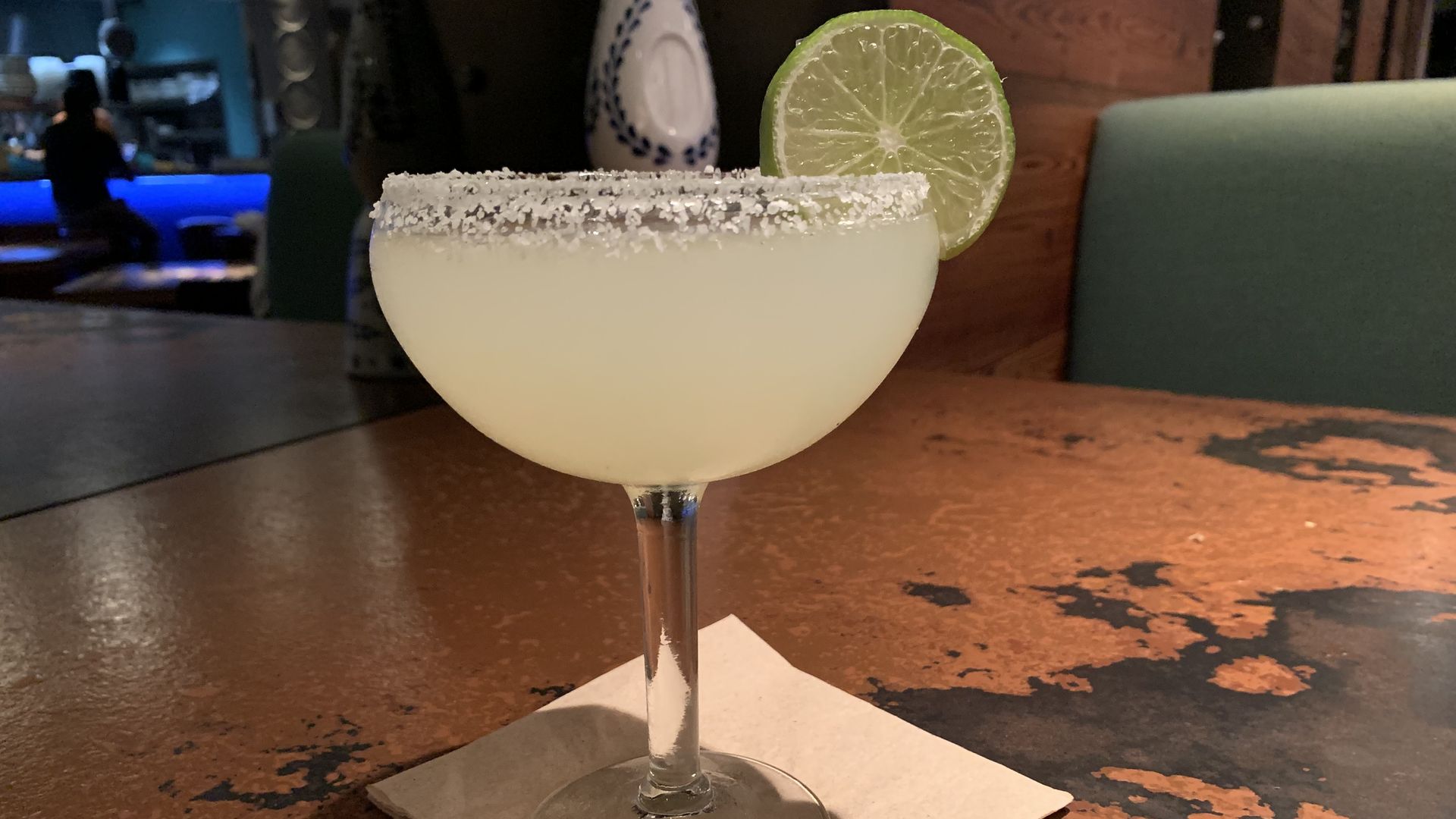 A chilled, green margarita in a goblet with salt and a lime on the rim.