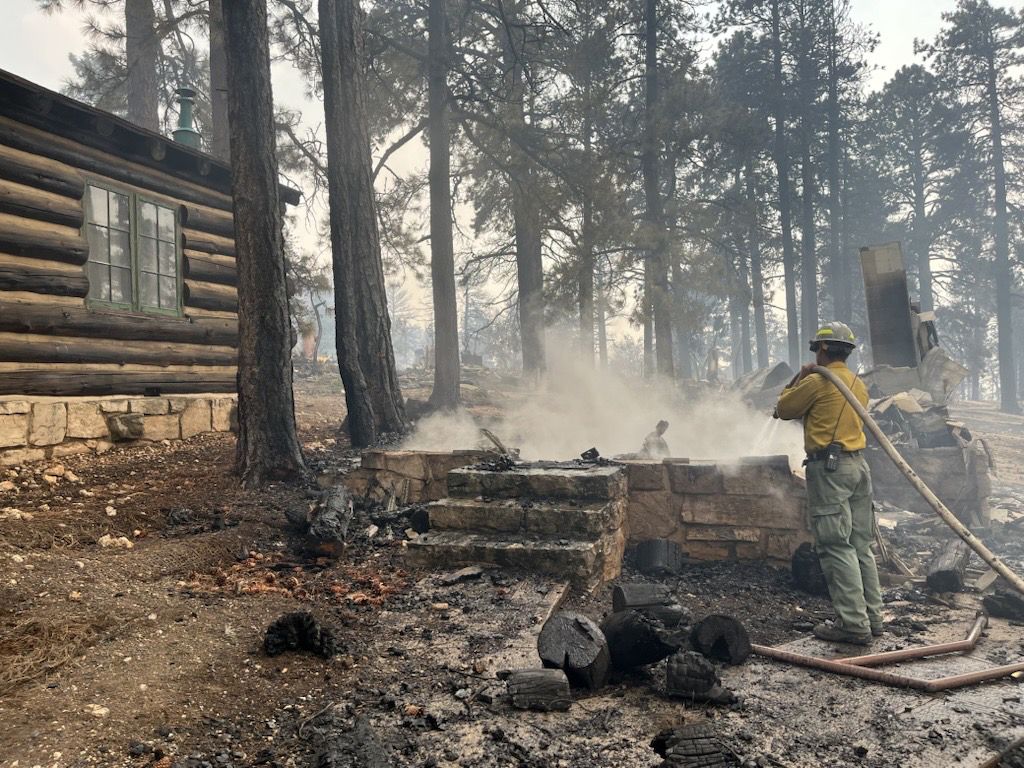 A firefighter stands near smoldering debris and active flames amid the charred remains of burned structures near the Grand Canyon Lodge at Grand Canyon National Park on July 13, 2025.