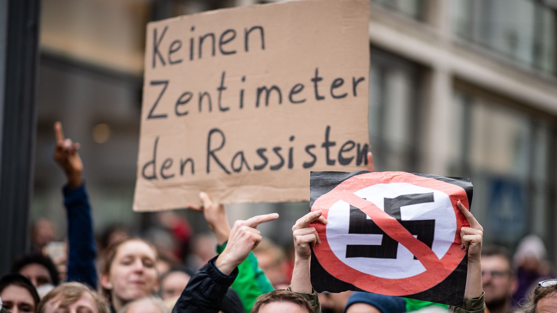 Protestors holding up signs including one that has a swastika crossed out. 