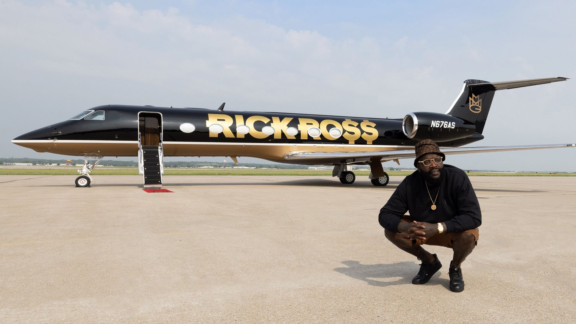 Rick Ross crouches in front of his black private plane that says "Rick Ross" in large gold letters