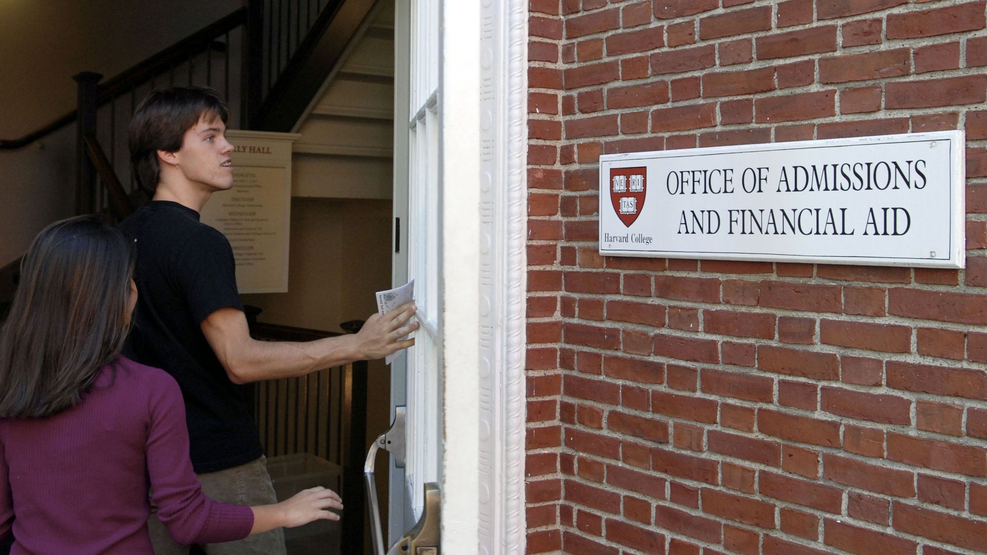 A young man and woman walking through a door at Harvard next to a sign saying Office of Admissions and Financial Aid 