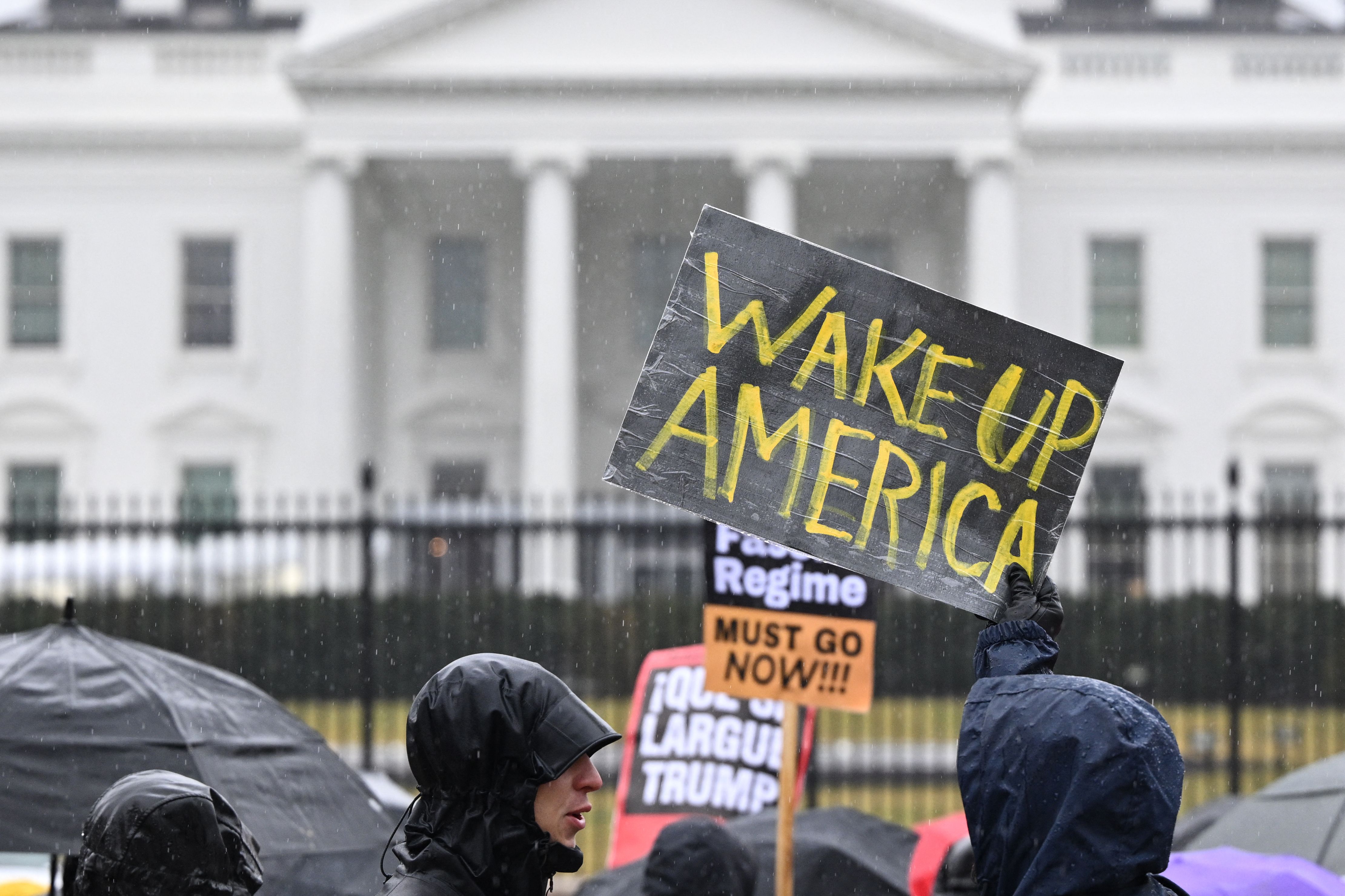 Protesters hold up signs in front of the White House. One sign says, "Wake Up America."