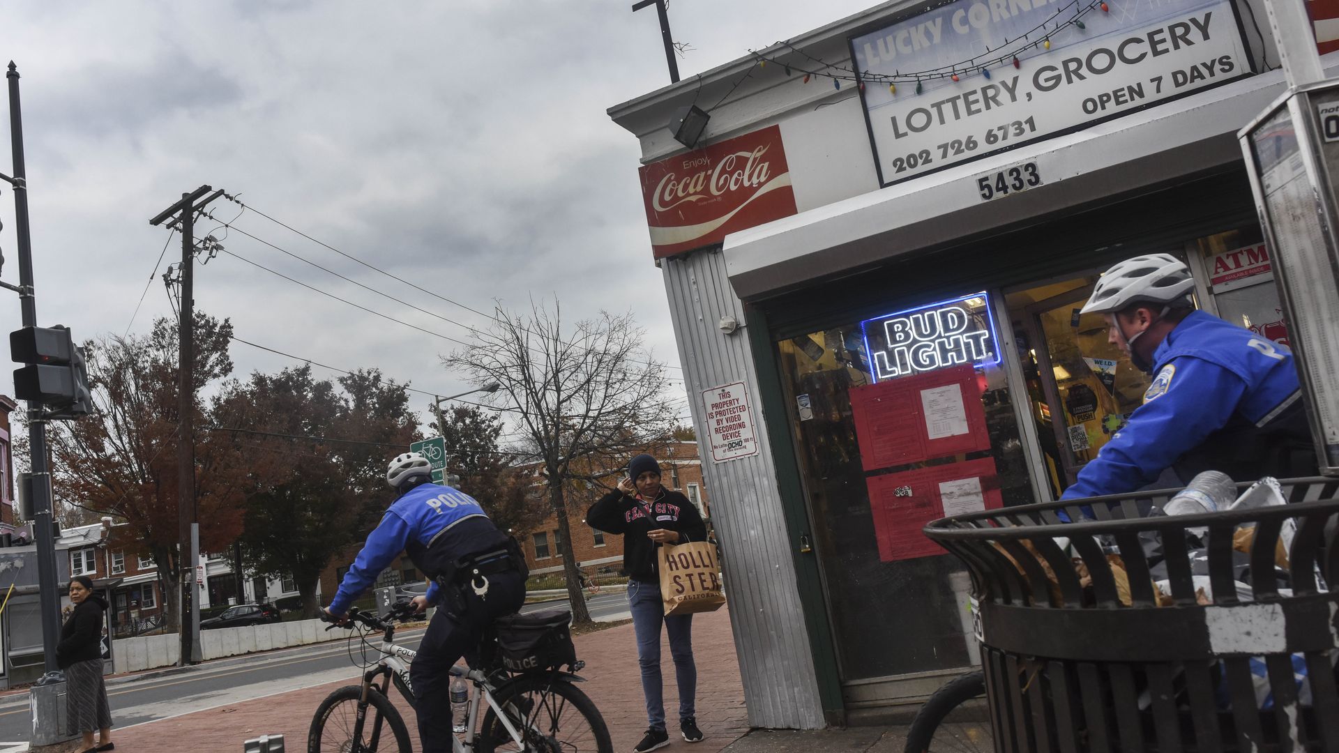 Two police officers are pictured riding on bicycles on the sidewalk by a corner store