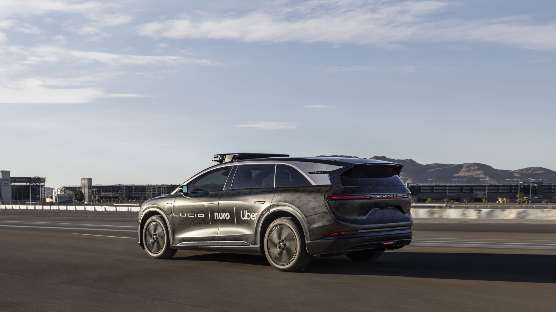Image of a silver-colored autonomous Lucid Gravity SUV on a test track, with the logos of Lucid, Nuro and Uber on it. 