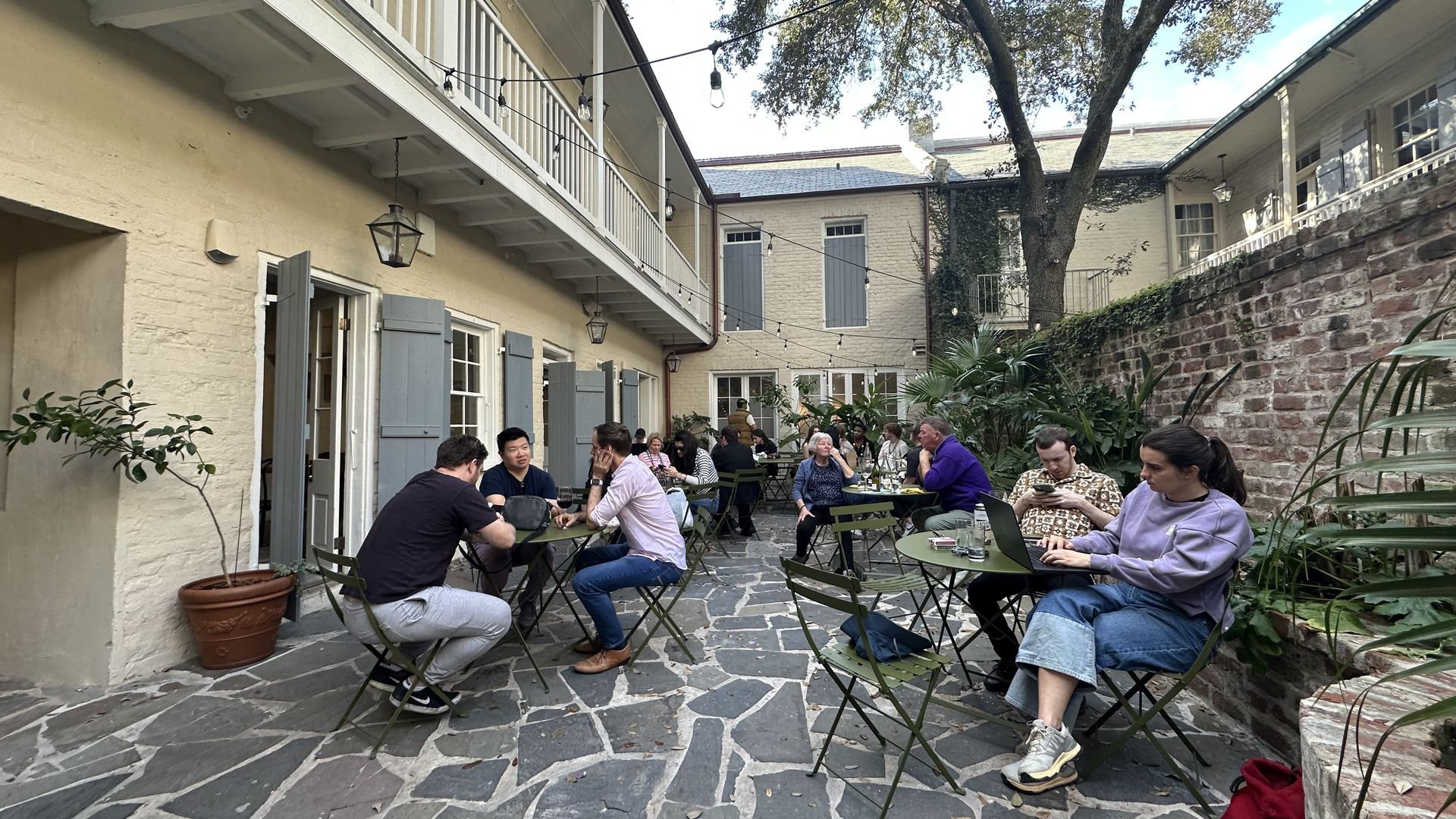 A French Quarter courtyard is crowded with guests at cafe tables.