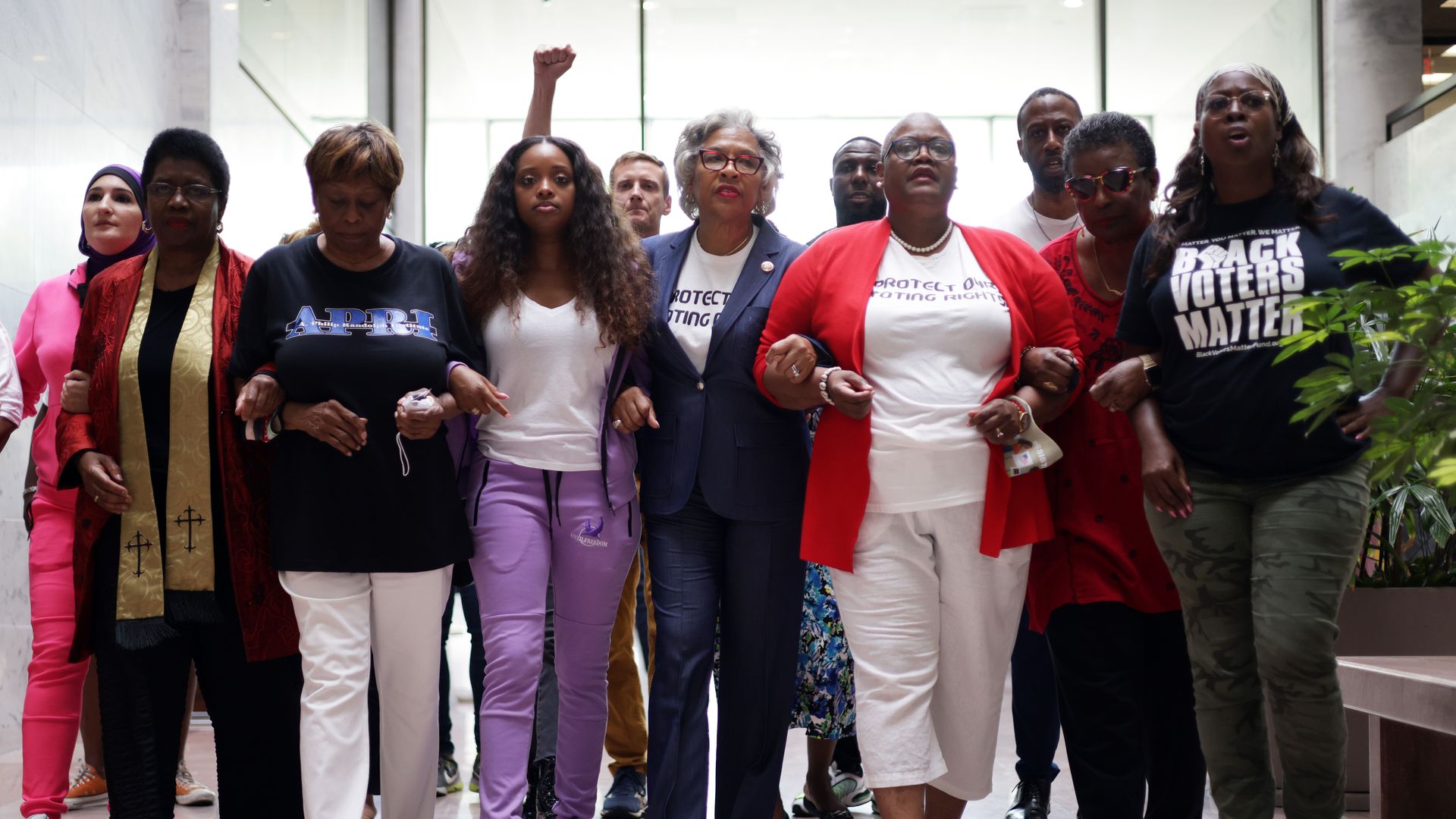 Photo of a group of women arm in arm walking through the lobby of a building and shouting