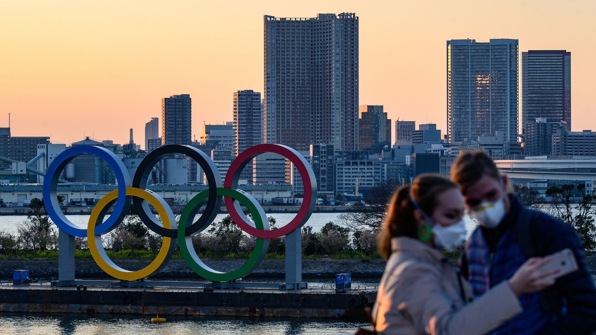 People wear face masks as they take pictures in front of the Olympic Rings at the Odaiba Seaside Park in Tokyo on March 6