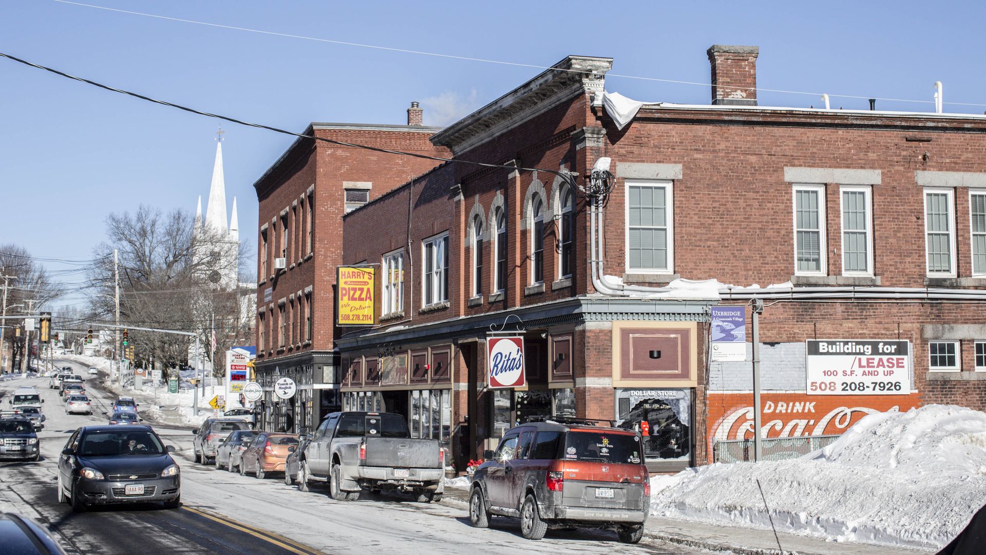 Alt text: Cars travel down a snow-lined Main Street in Uxbridge, Mass.