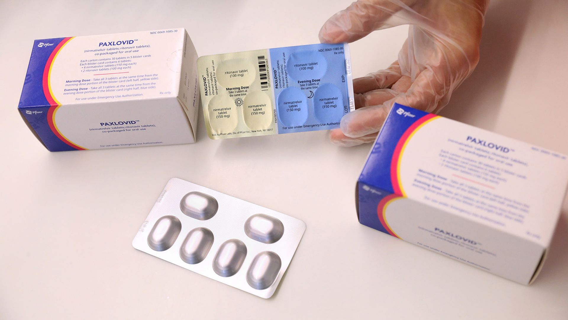 A hand wearing a medical glove handles boxes of Paxlovid.