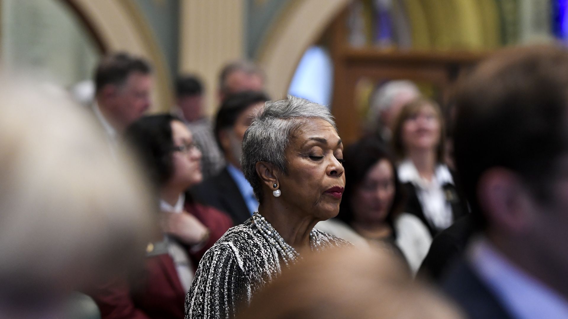 State Rep. Janet Buckner stands on the House floor with her eyes closed.