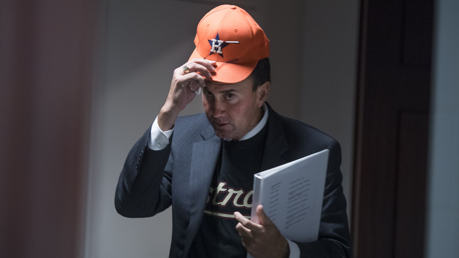 This image shows Olson donning an orange baseball cap while holding a binder and walking.