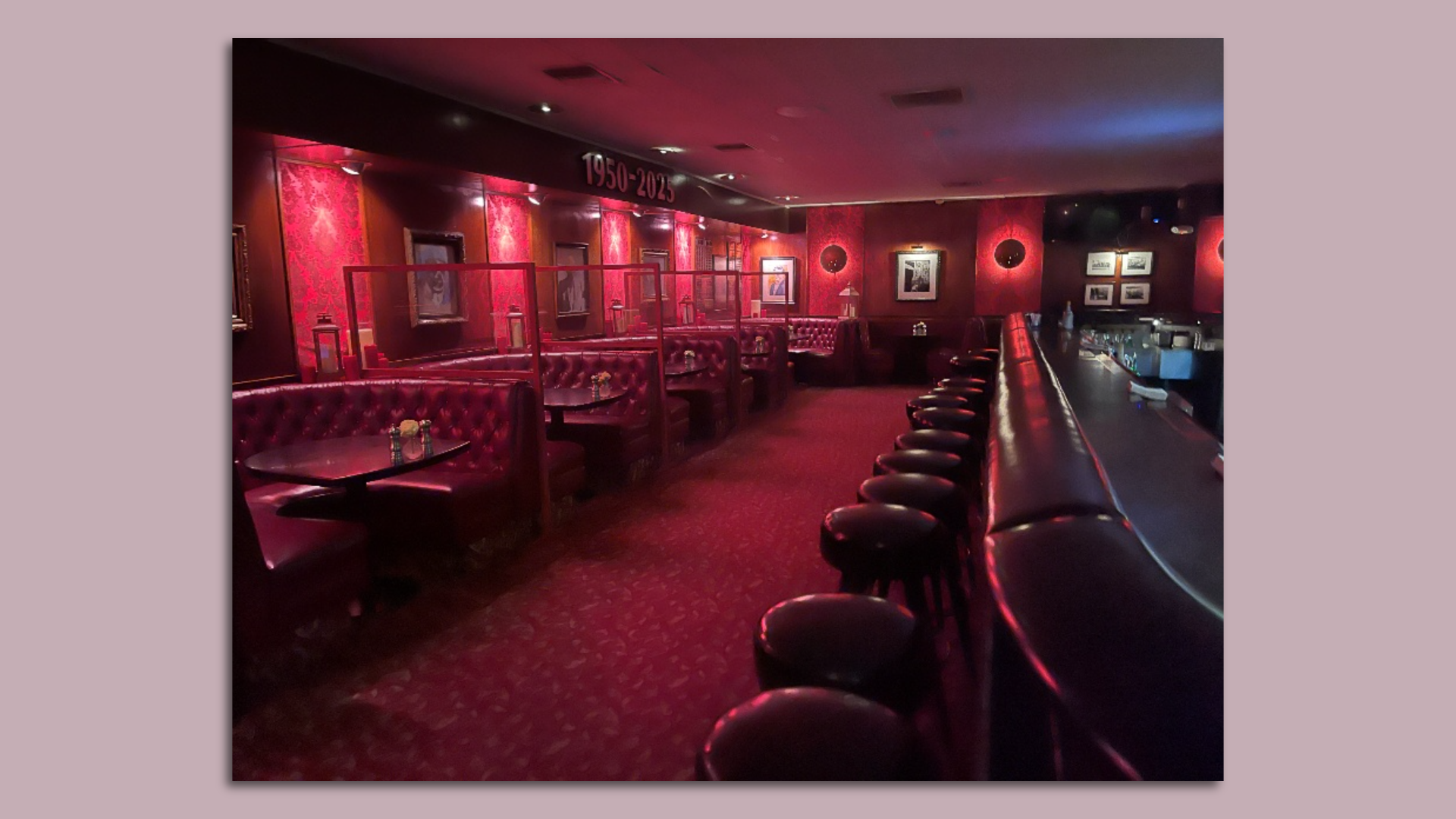 The inside of a darkly lit restaurant with a row of plush leather booths on one side and a bar with a row of barstools on the other.