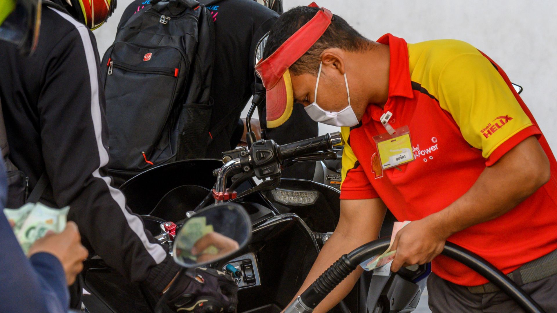 A Shell employee in Bangkok filling up someone's gas tank.