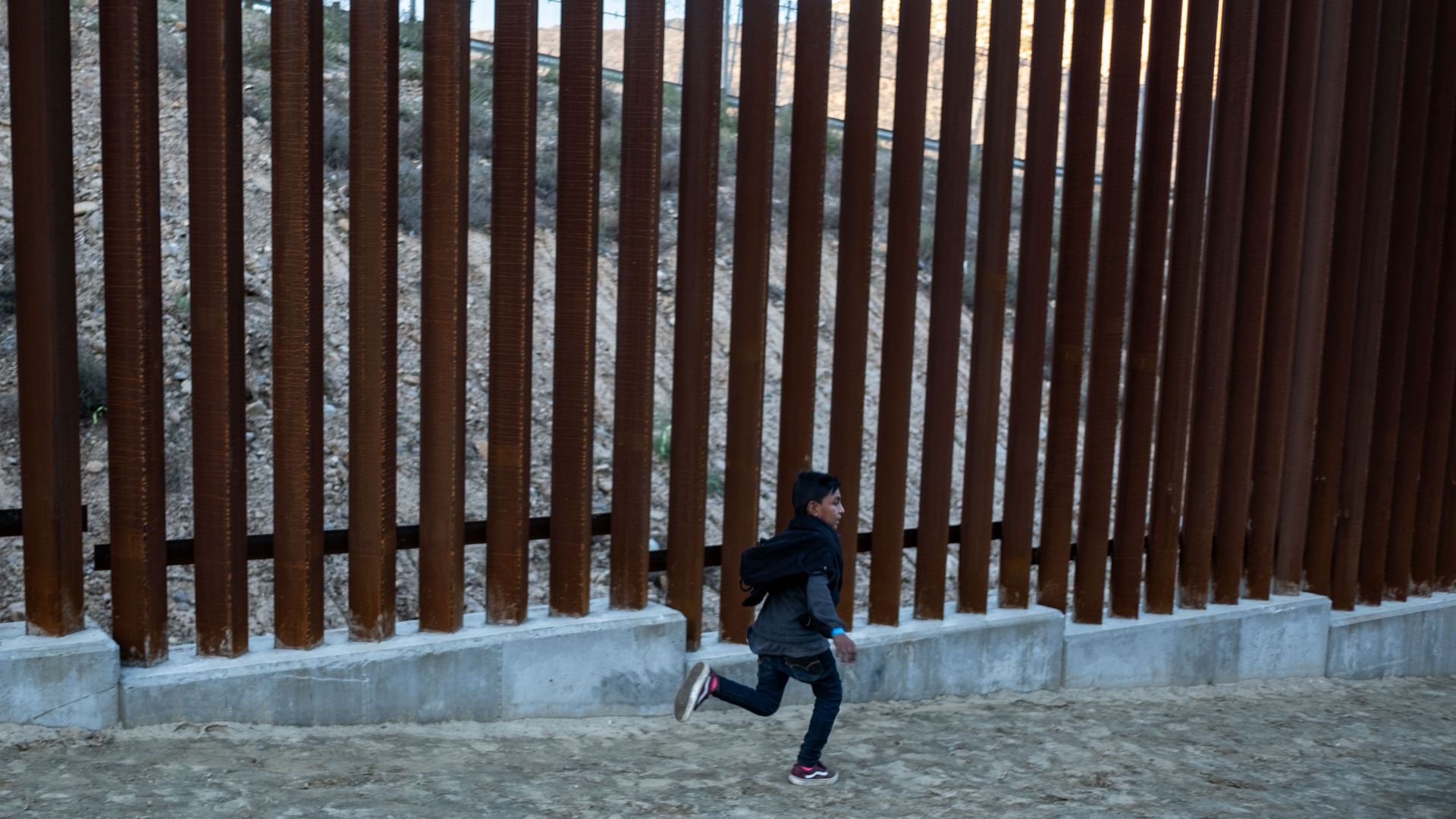 Boy runs near border wall.