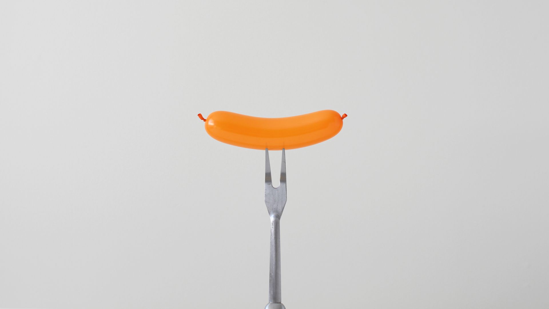 A balloon shaped like a hot dog is skewered on a metal fork.