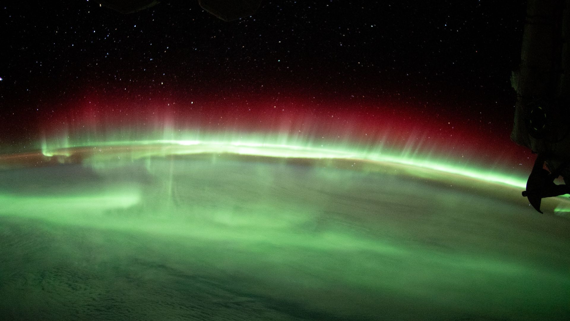 Green auroras dance above Earth's surface as seen from above on the International Space Station