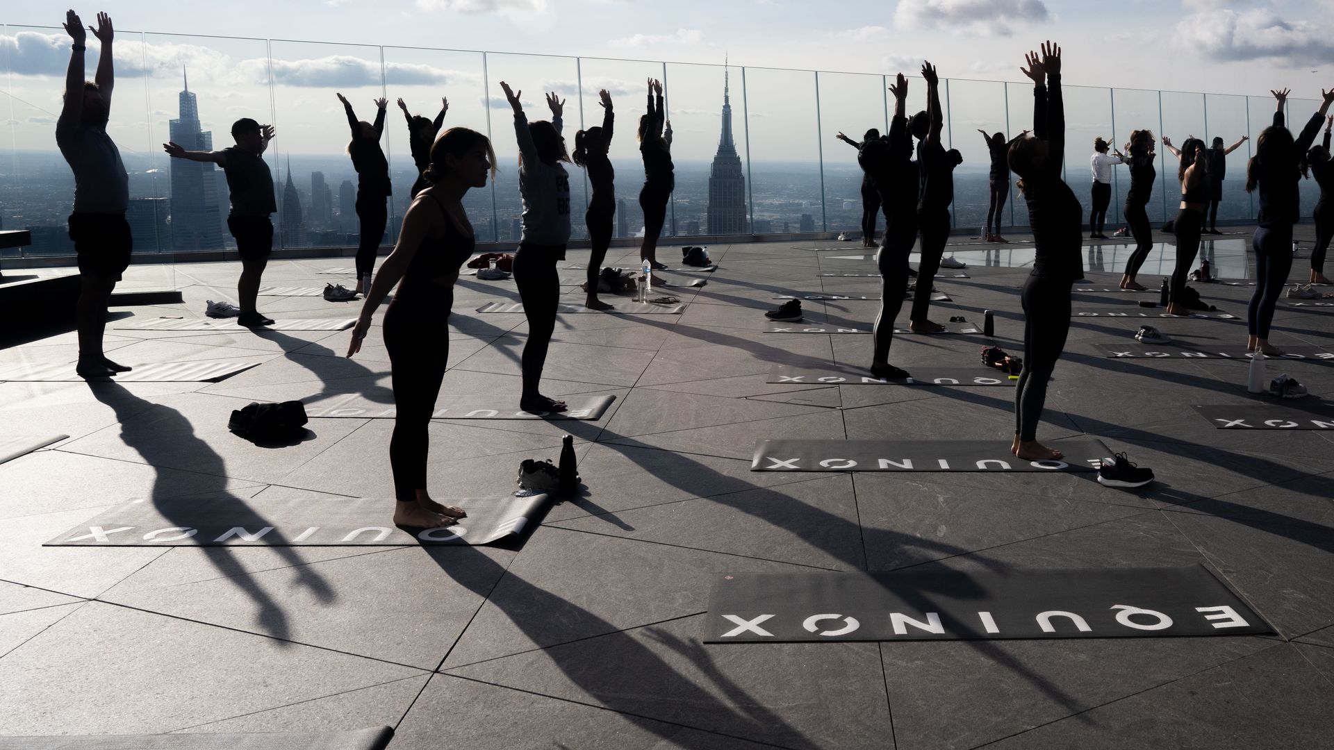 Yoga participants reach toward the sky on a skyscraper