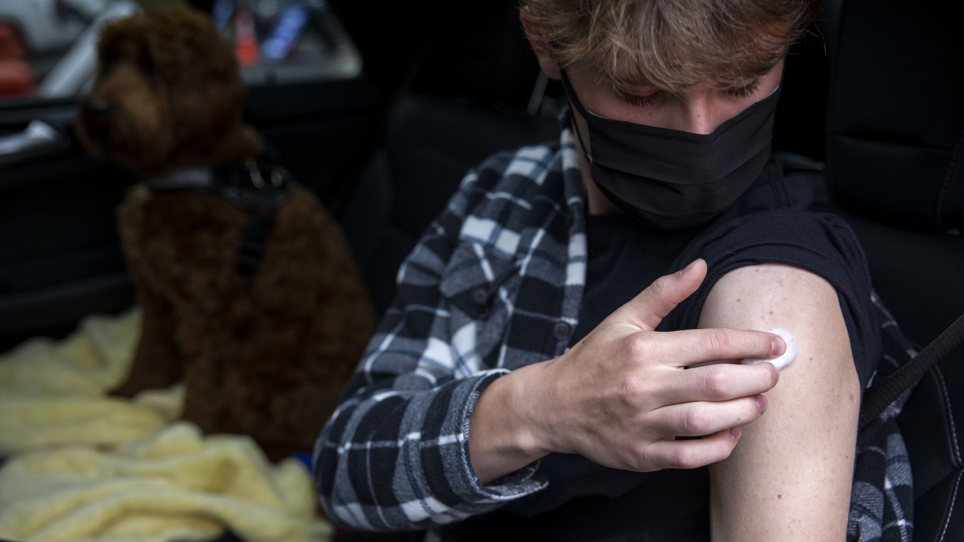 A boy holds a cotton ball against his upper arm with his shit sleeve rolled up. 