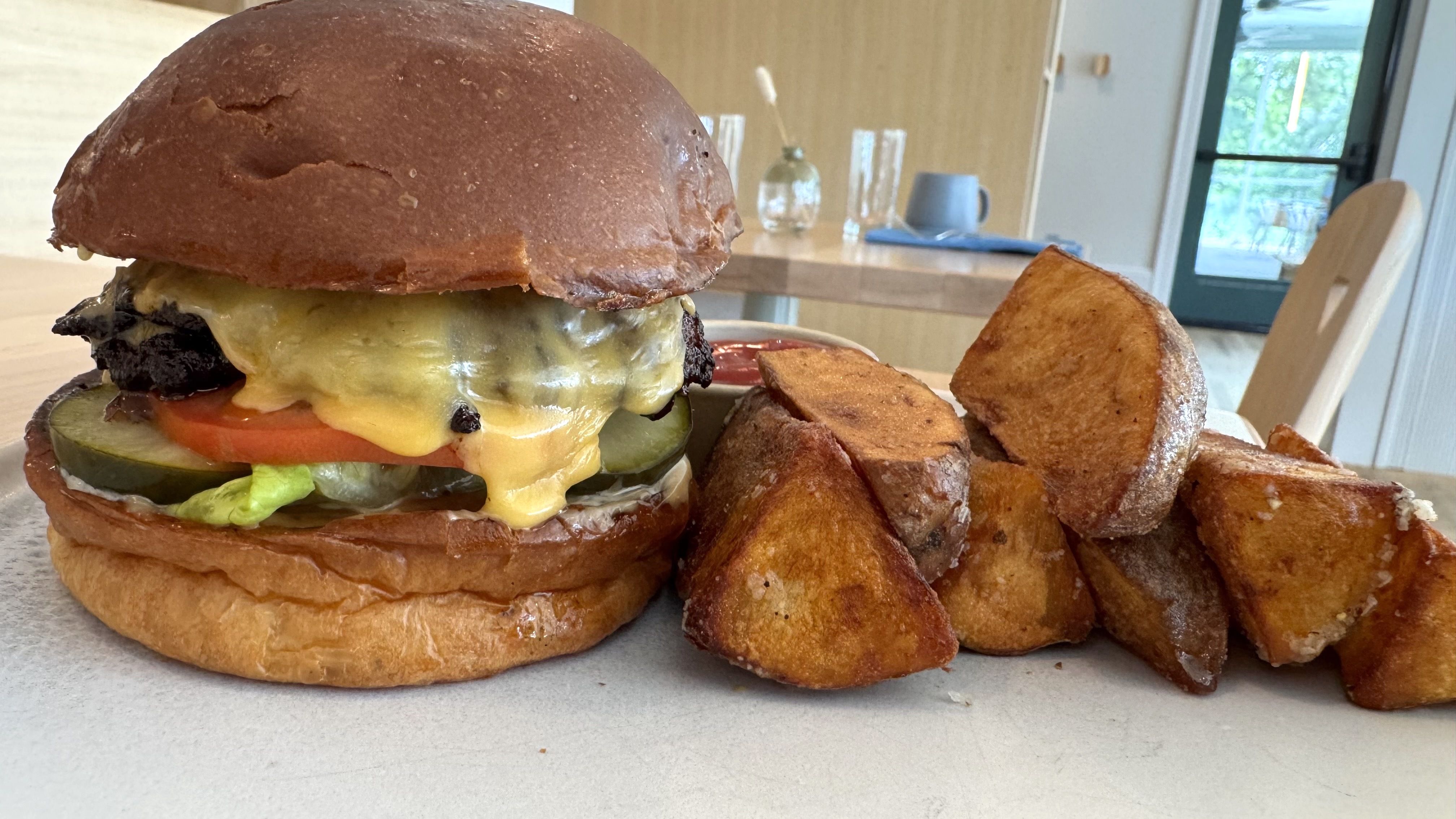 Cheeseburger with lettuce, tomato, pickles, and crispy bun served with thick, golden potato wedges and ketchup.