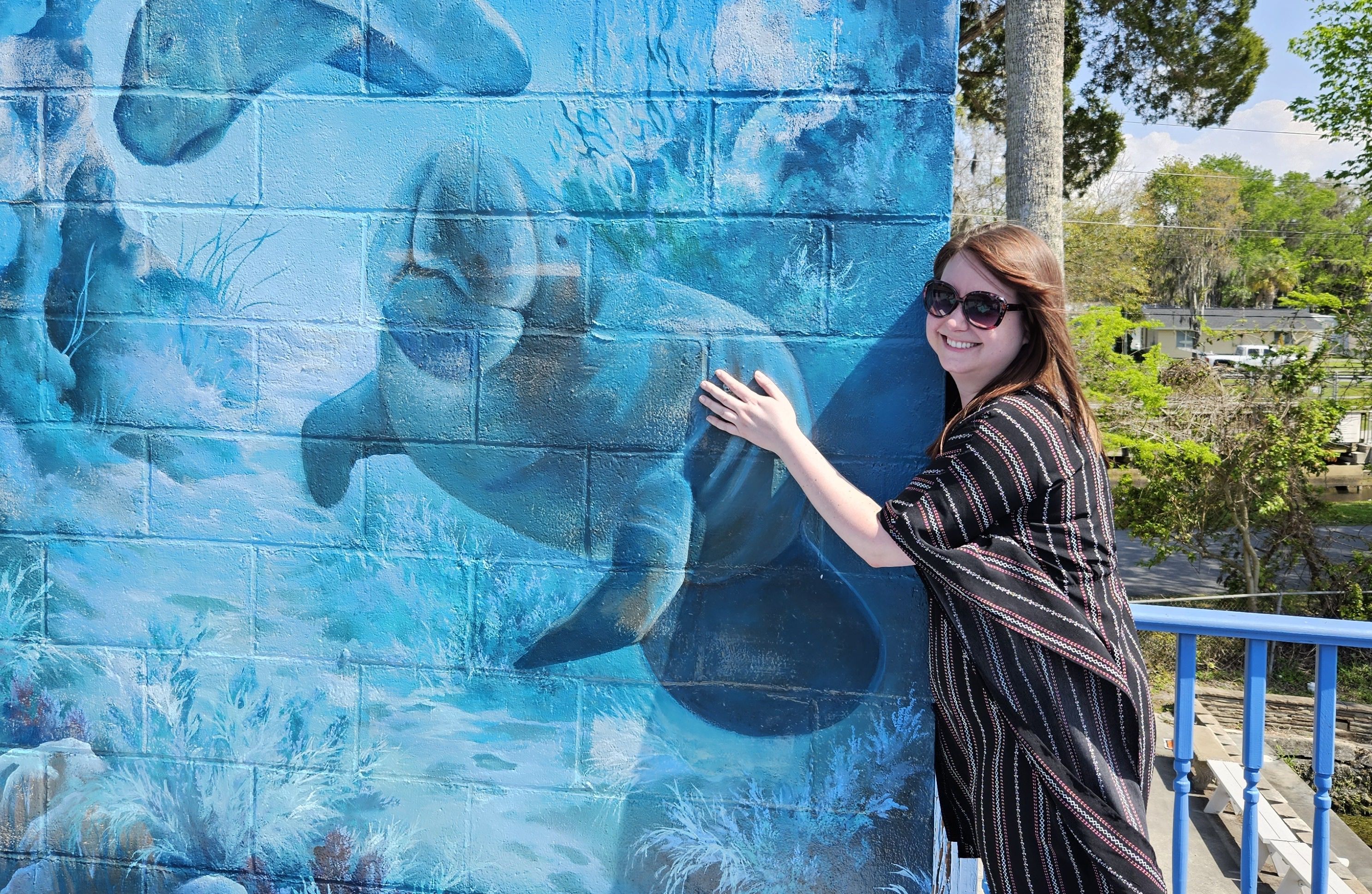 Alissa poses next to a manatee mural on a brick wall