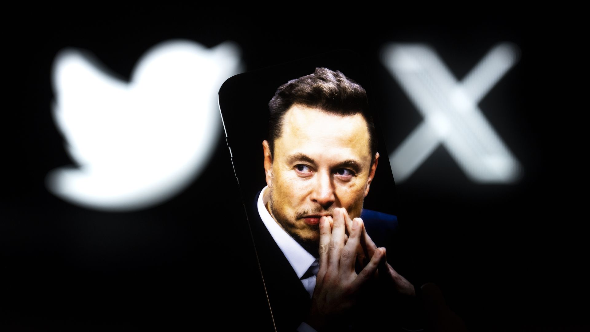 An effigy of Elon Musk is seen on a mobile device with the X and Twitter lgoso in the background in this photo illustration on 23 July, 2023 in Warsaw, Poland.
