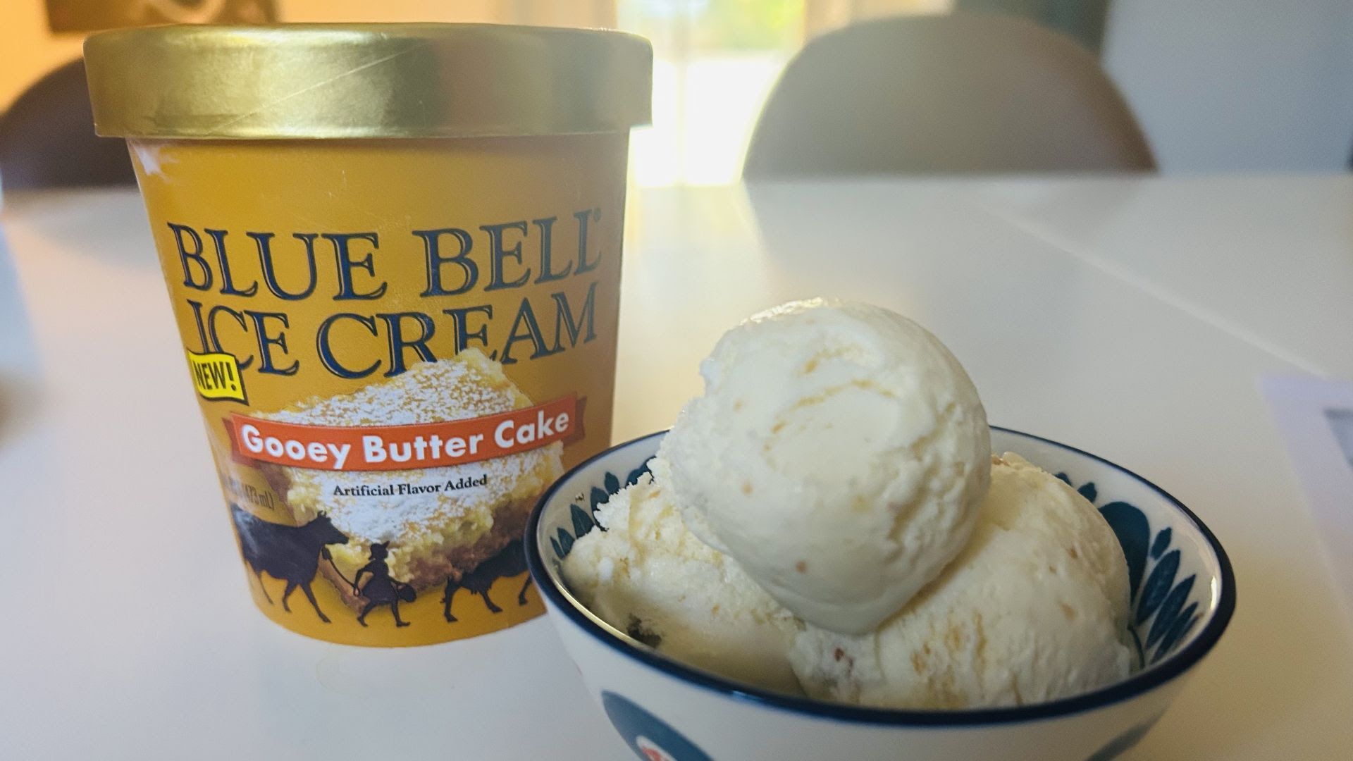 A golden tub of ice cream in Gooey Butter Cake flavor from Blue Bell, next to a bowl of the ice cream.