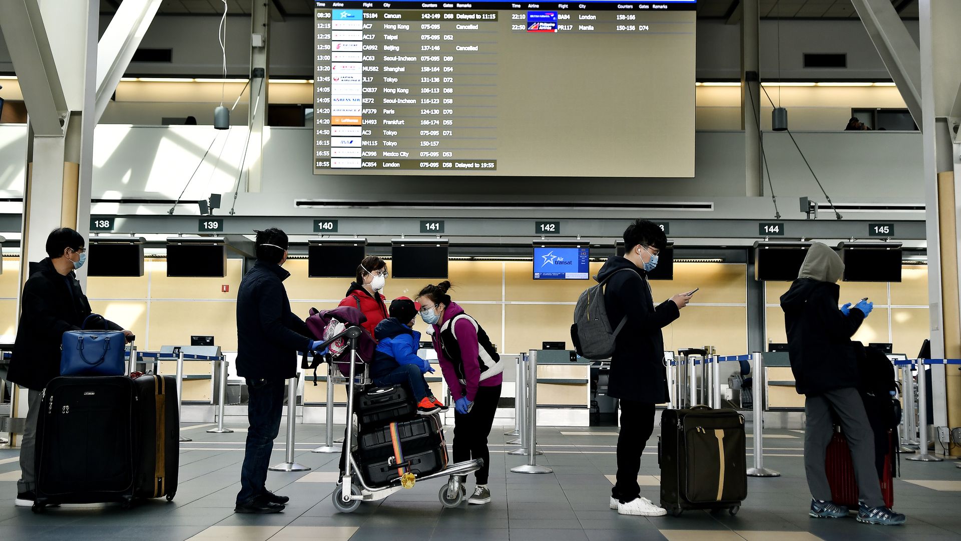Travelers wearing protective masks wait in line in the international departures area in Vancouver International Aiport (YVR) in Vancouver, British Columbia, Canada
