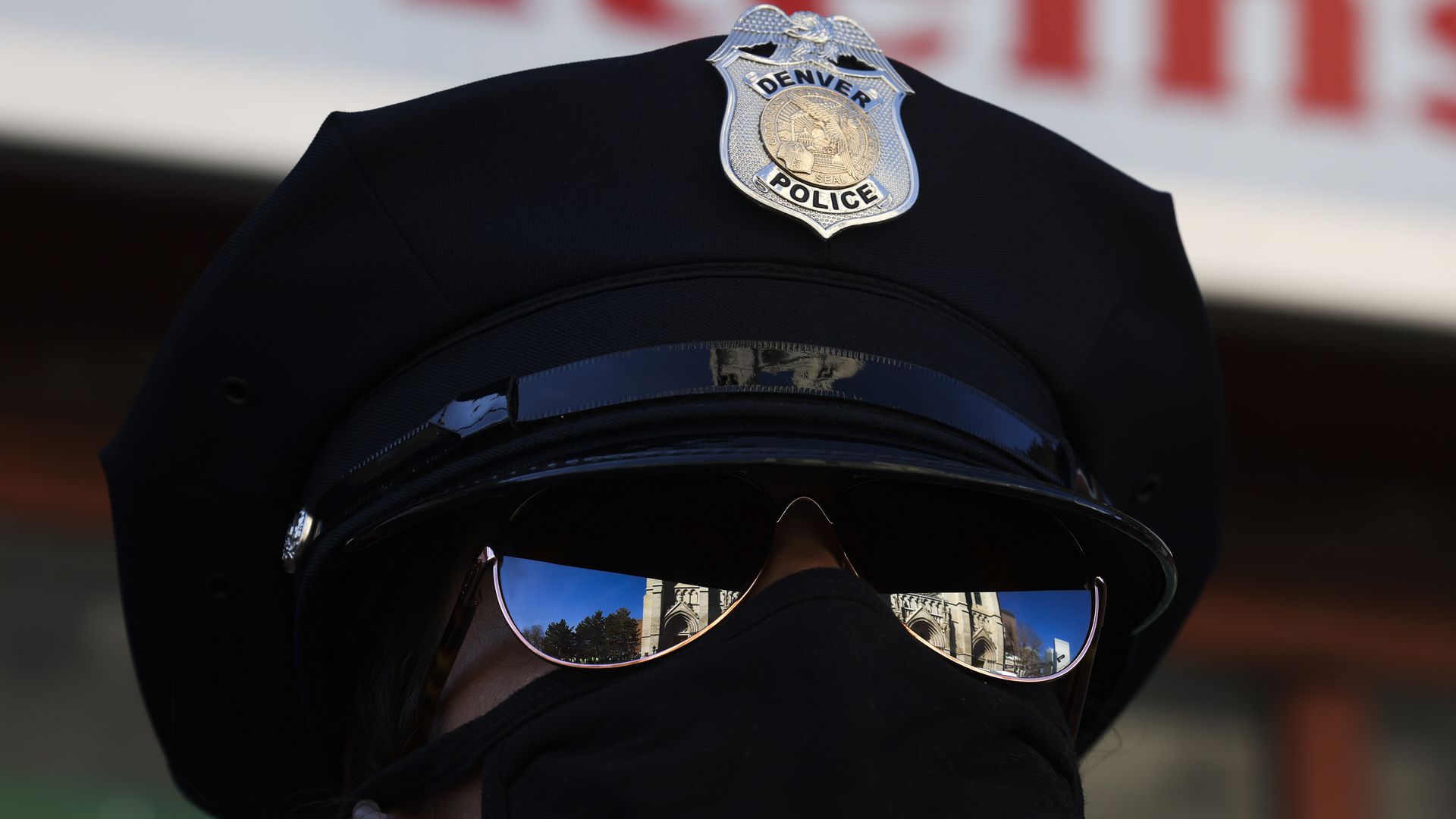 A close-up photo of a Denver police officer wearing a uniform hat, sunglasses and COVID-19 face mask.