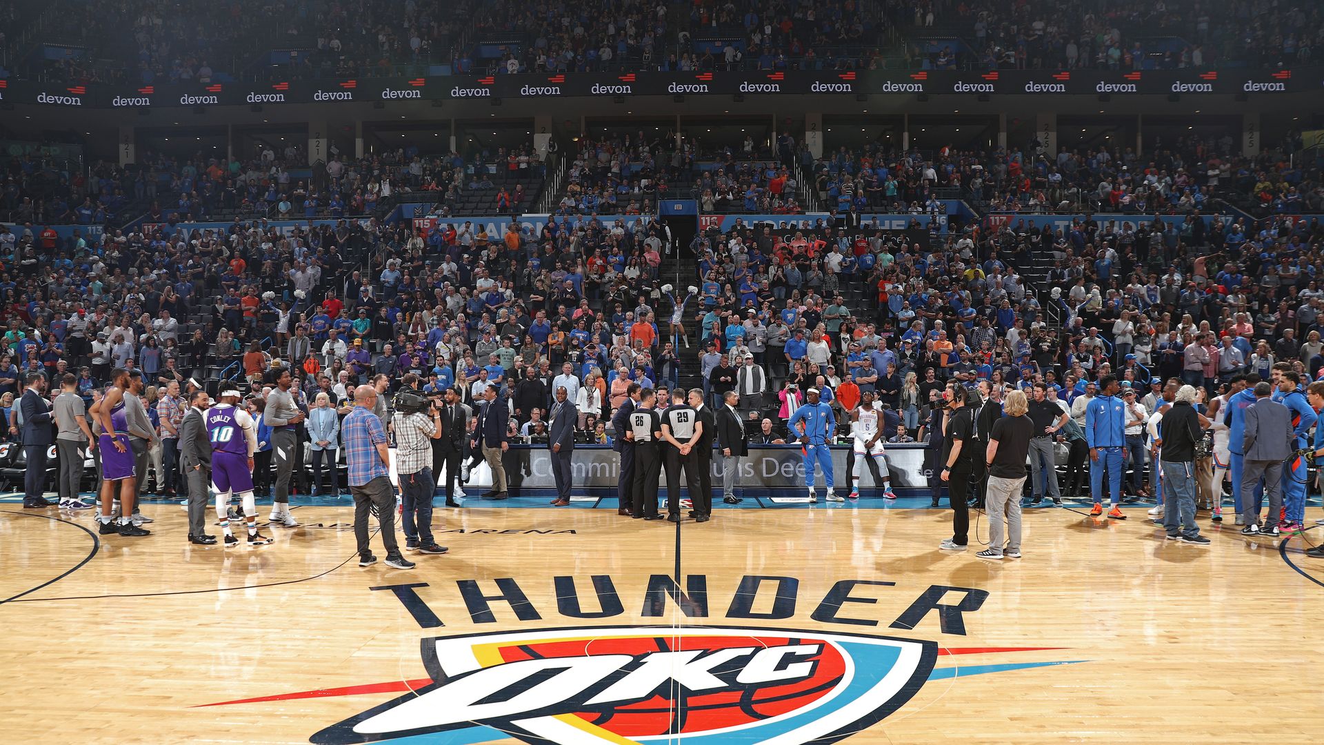 A basketball arena with NBA players and referees standing around and talking