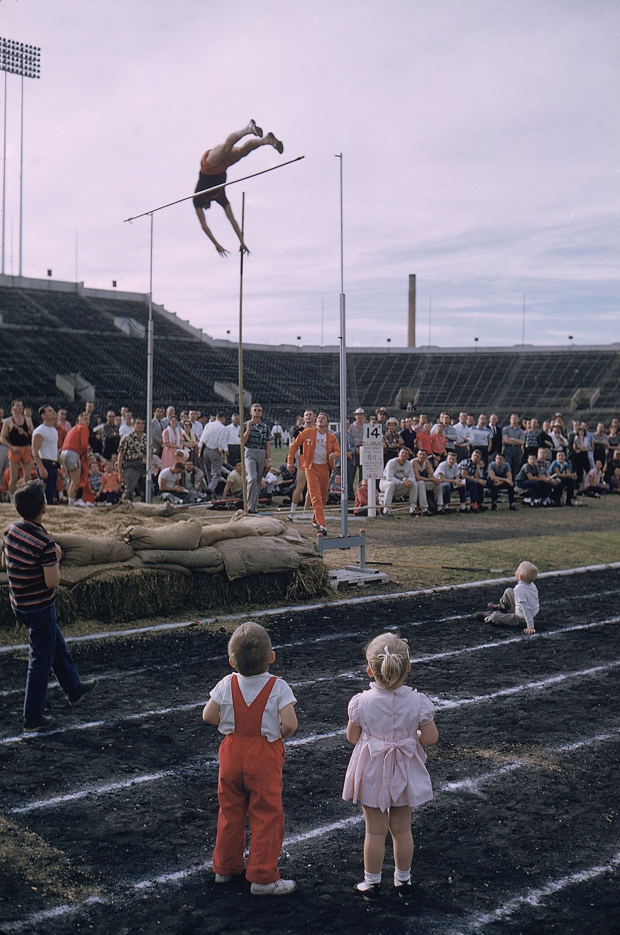 An image of two children in the foreground, watching a man compete in track.